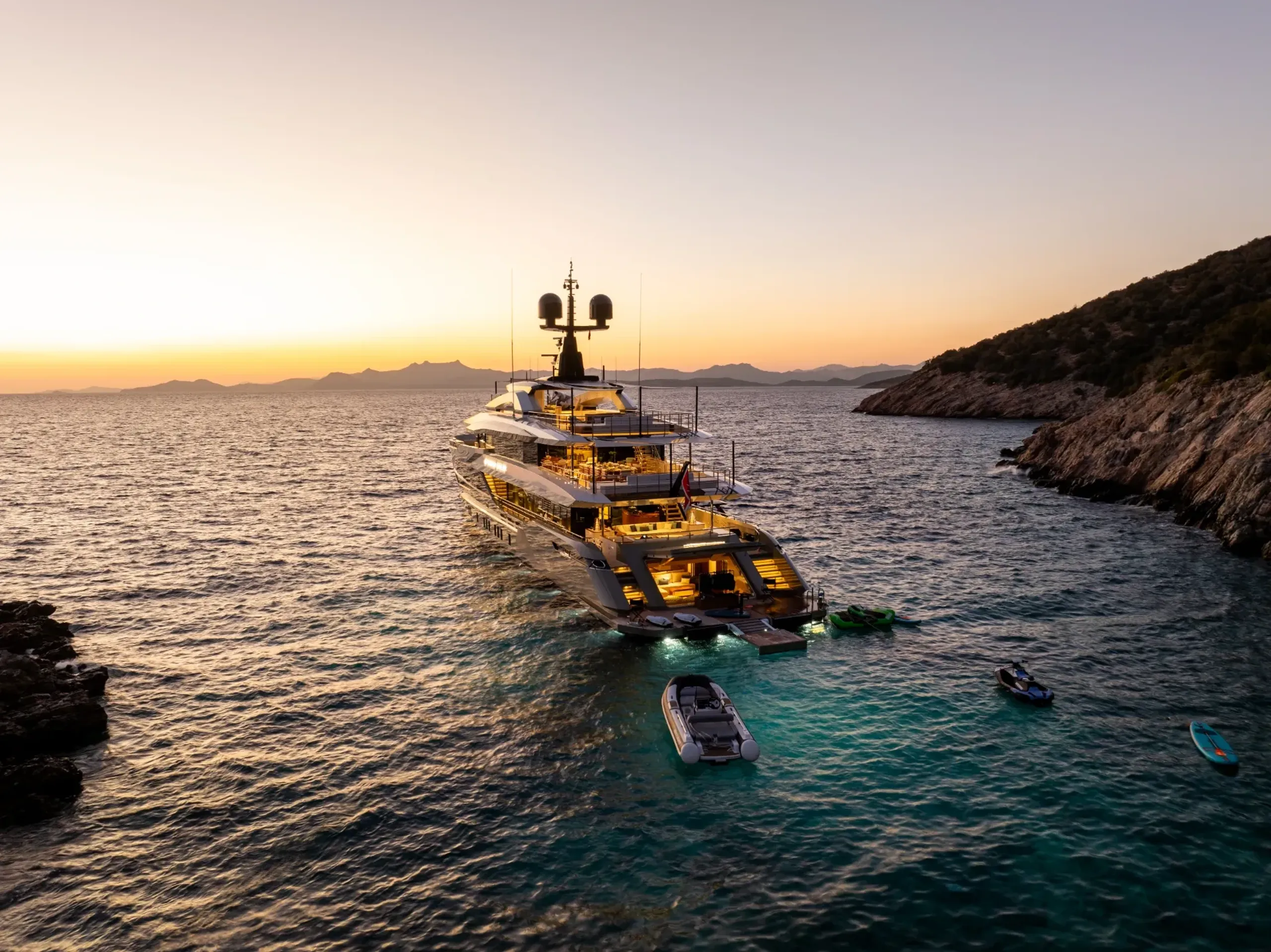 Superyacht anchored at sunset with tender and water toys nearby