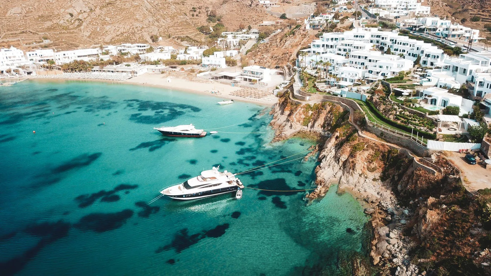 Yachts anchored in turquoise water off a Greek island coastline