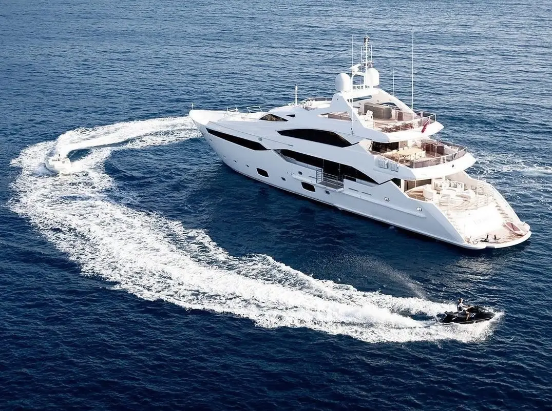 Superyacht cruising at sea with a jet ski circling nearby.