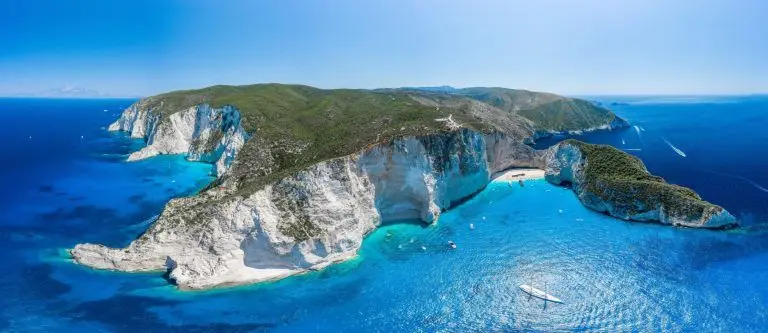 Aerial view of a turquoise bay with cliffs and boats at anchor.