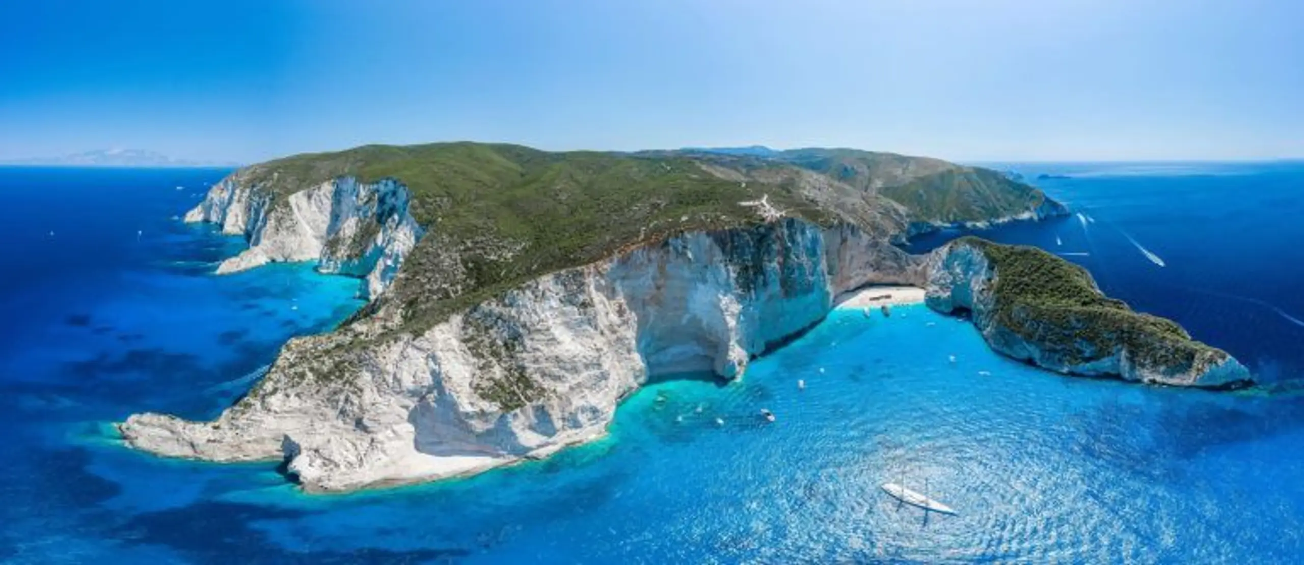 Aerial view of a turquoise bay with cliffs and boats at anchor.