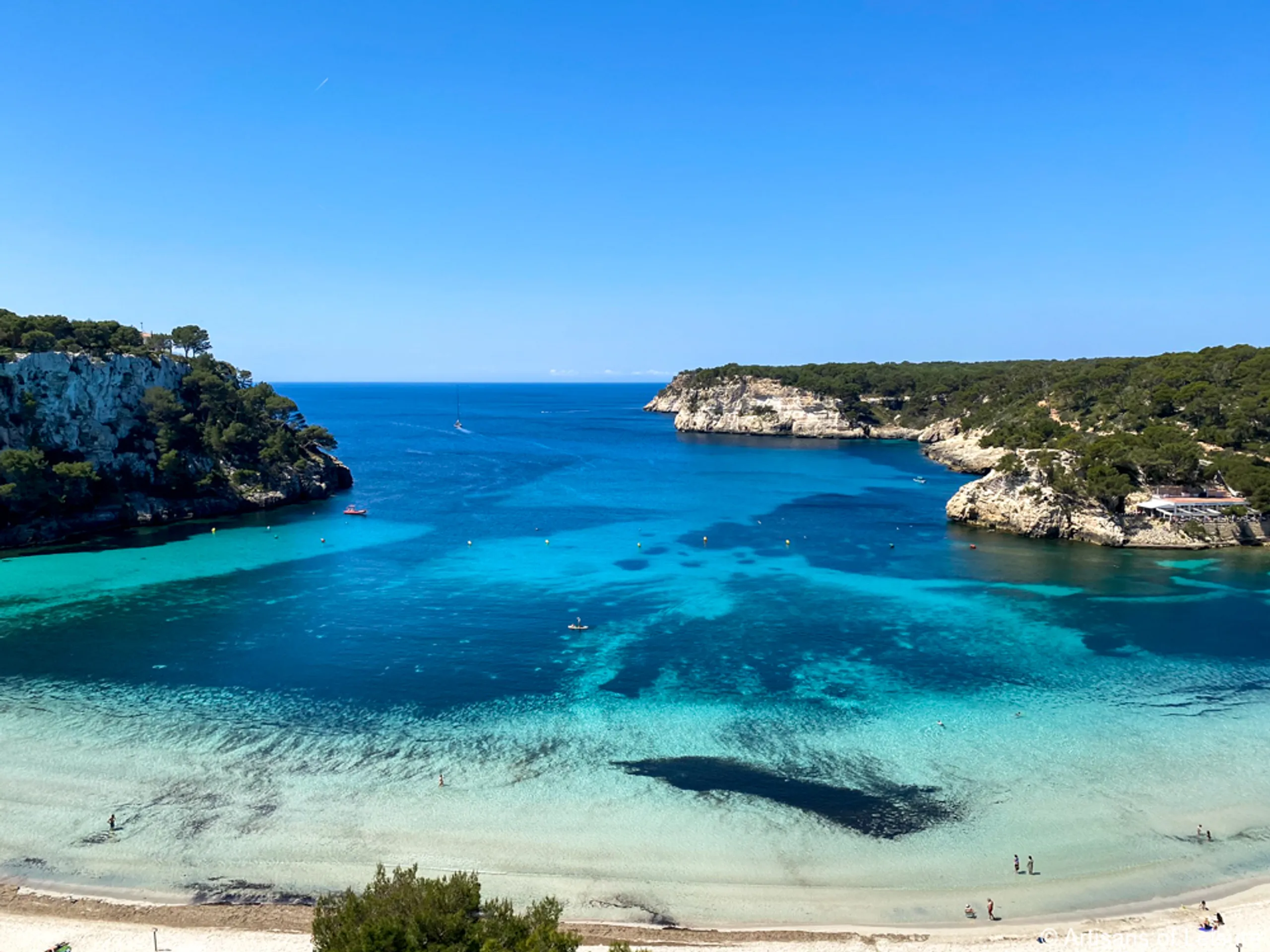 Turquoise bay and white sand beach in Menorca with cliffs and pine trees