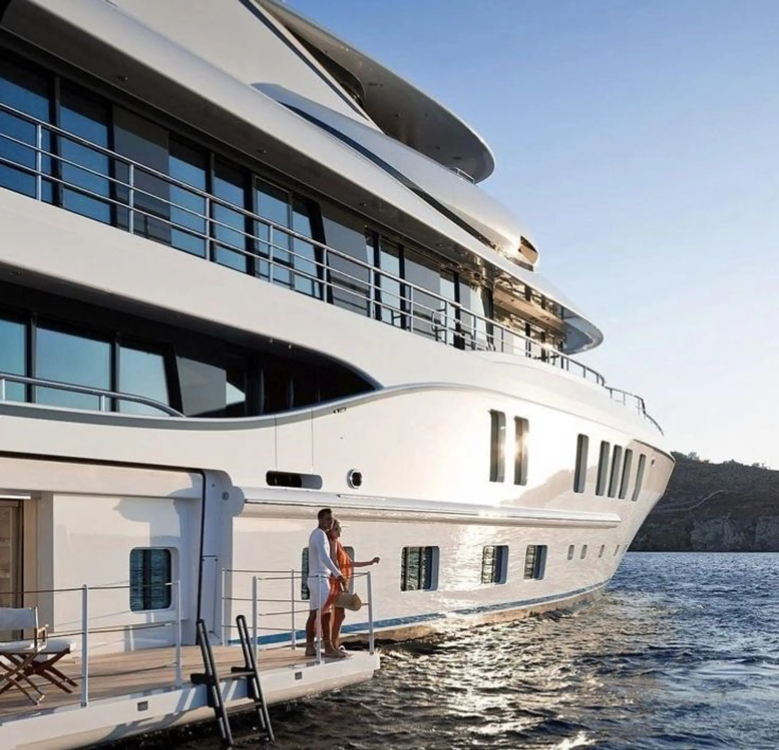 A couple on the swim platform of a superyacht at golden hour