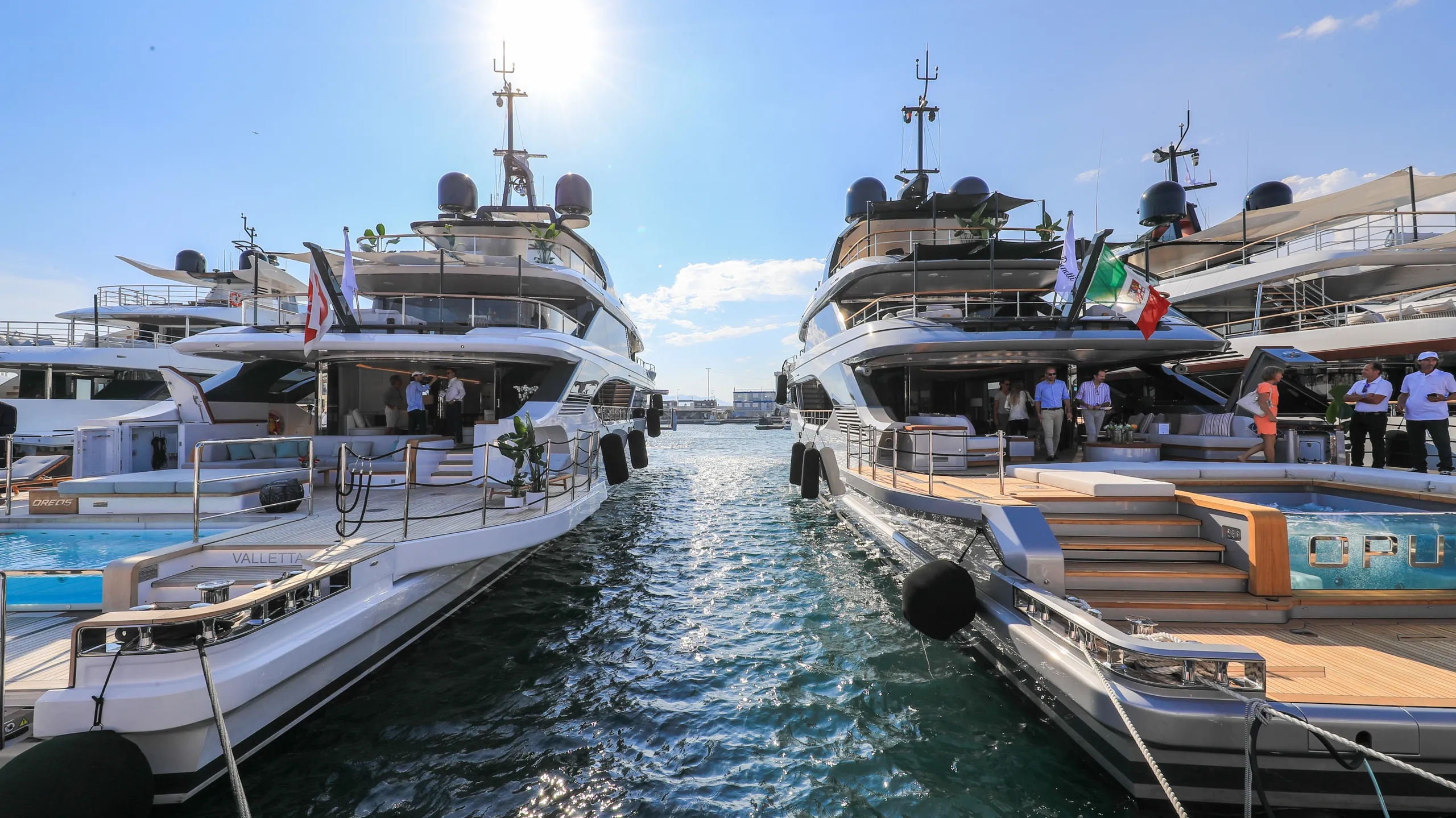 Two superyachts moored side by side with crew and tender alongside