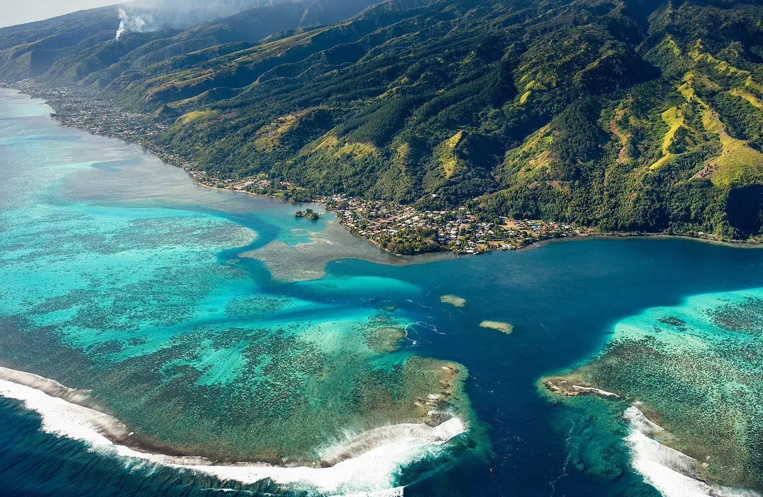Aerial view of French Polynesia with turquoise lagoon, coral reef, and lush mountain coastline