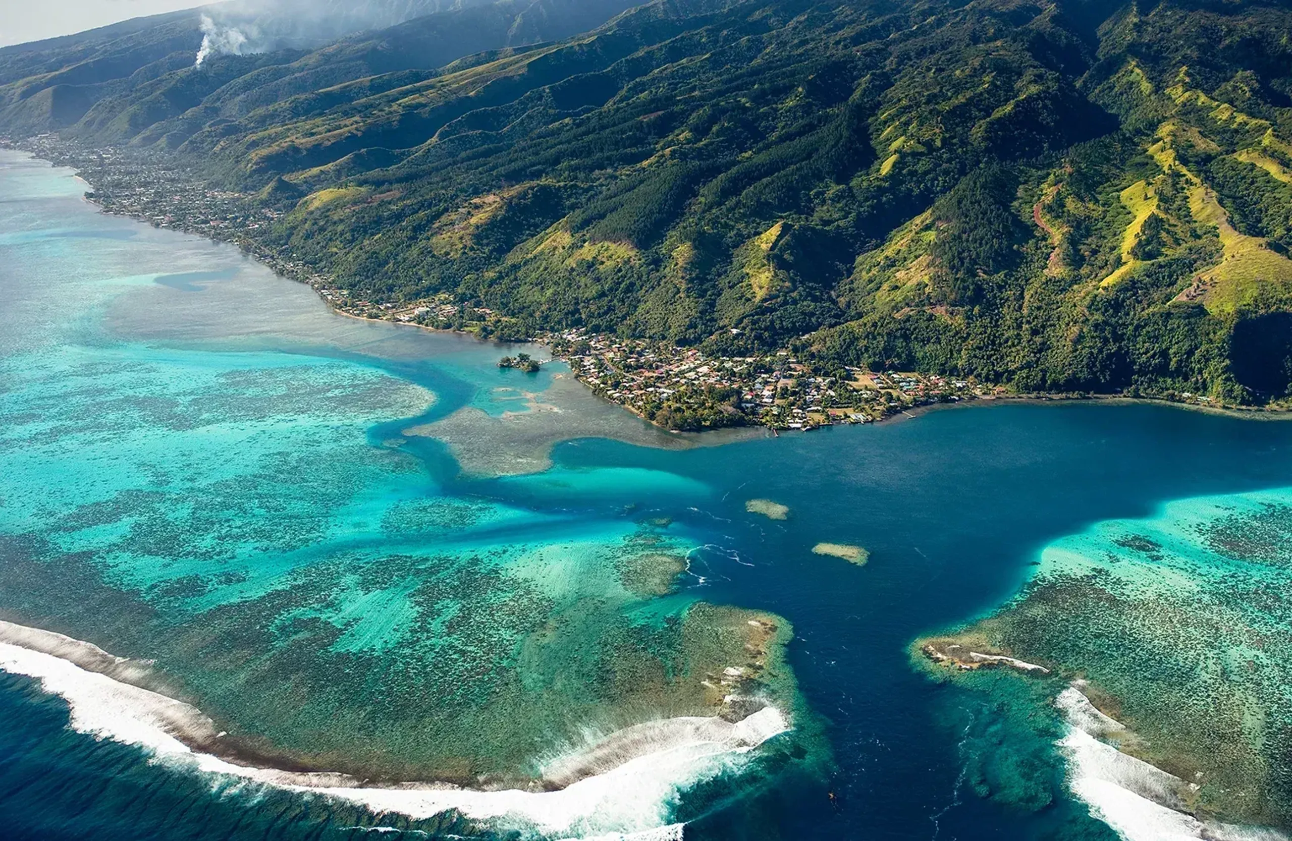Aerial view of French Polynesia with turquoise lagoon, coral reef, and lush mountain coastline