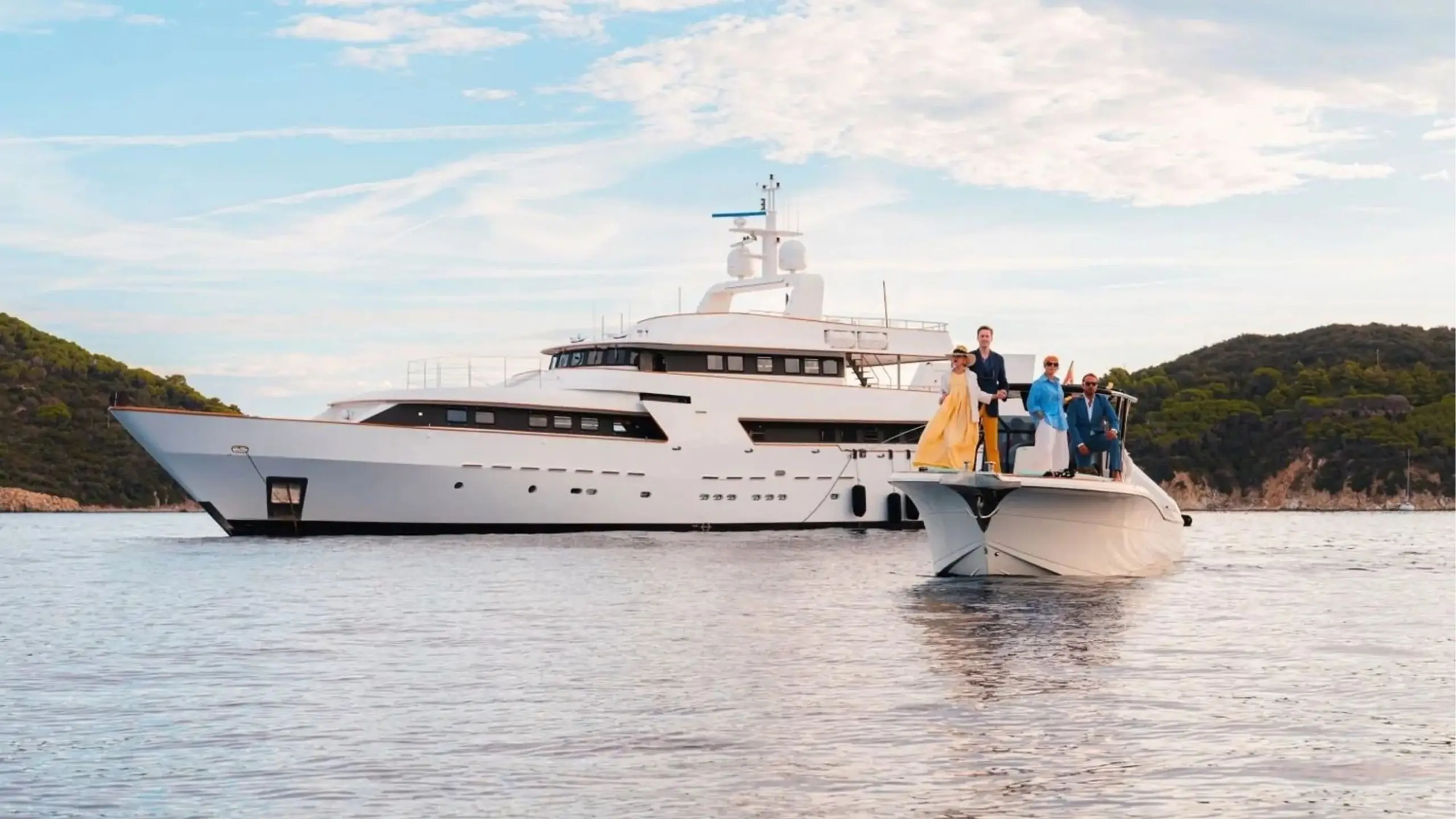 Guests on a tender approaching a superyacht at anchor in a calm bay