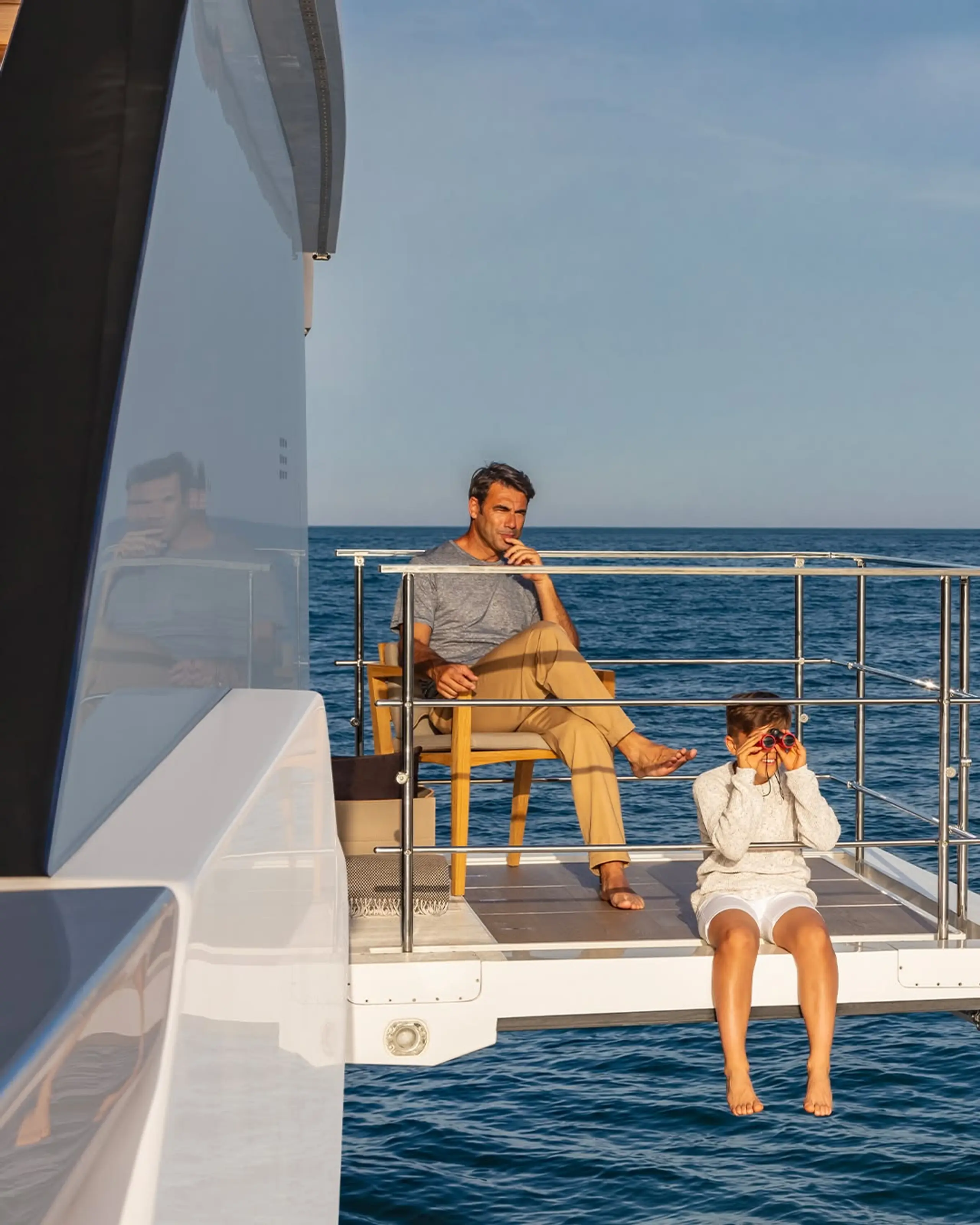 Man and child relaxing on the aft deck of a yacht at sea.