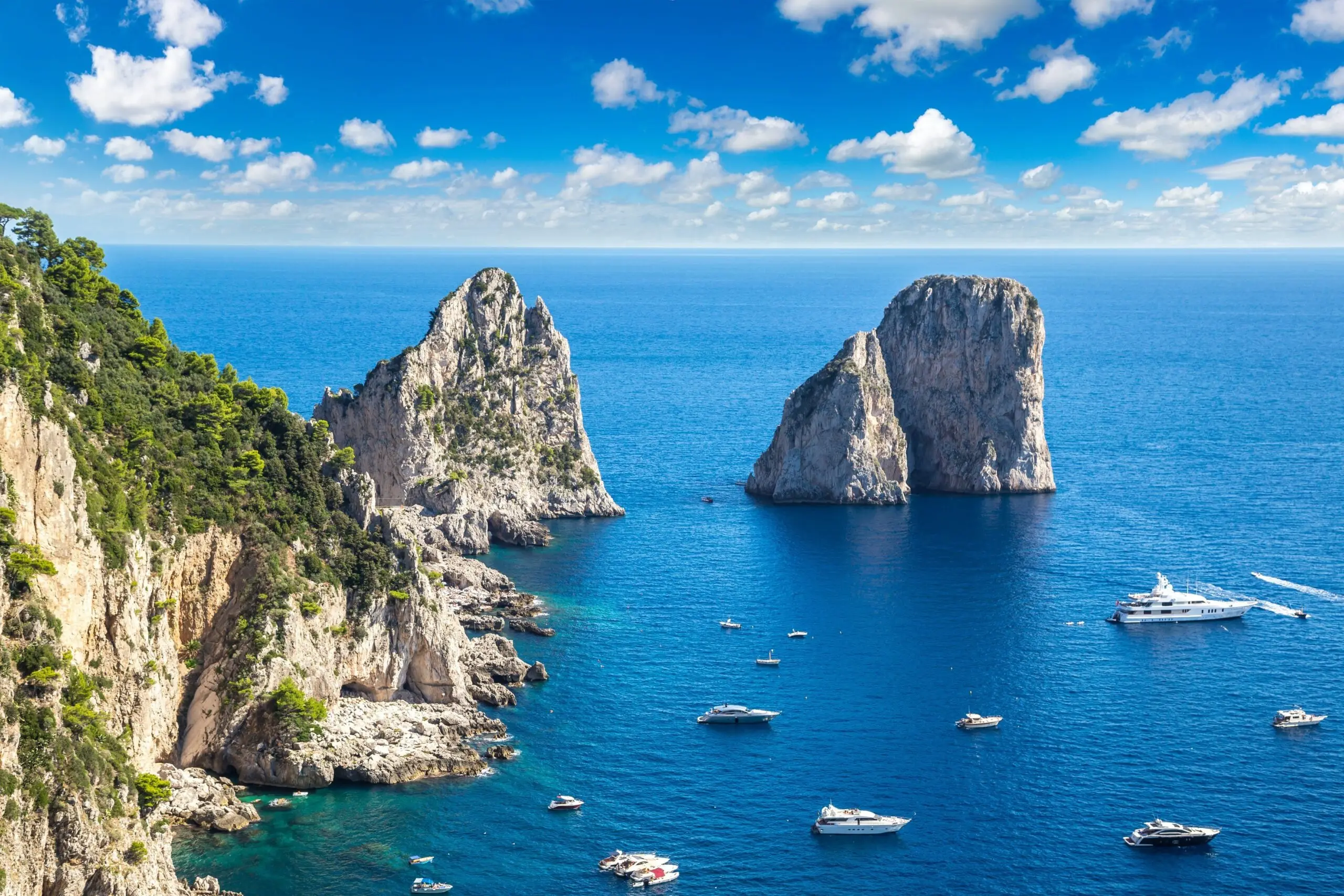 Luxury yachts cruising off Capri with the Faraglioni rocks in the background.