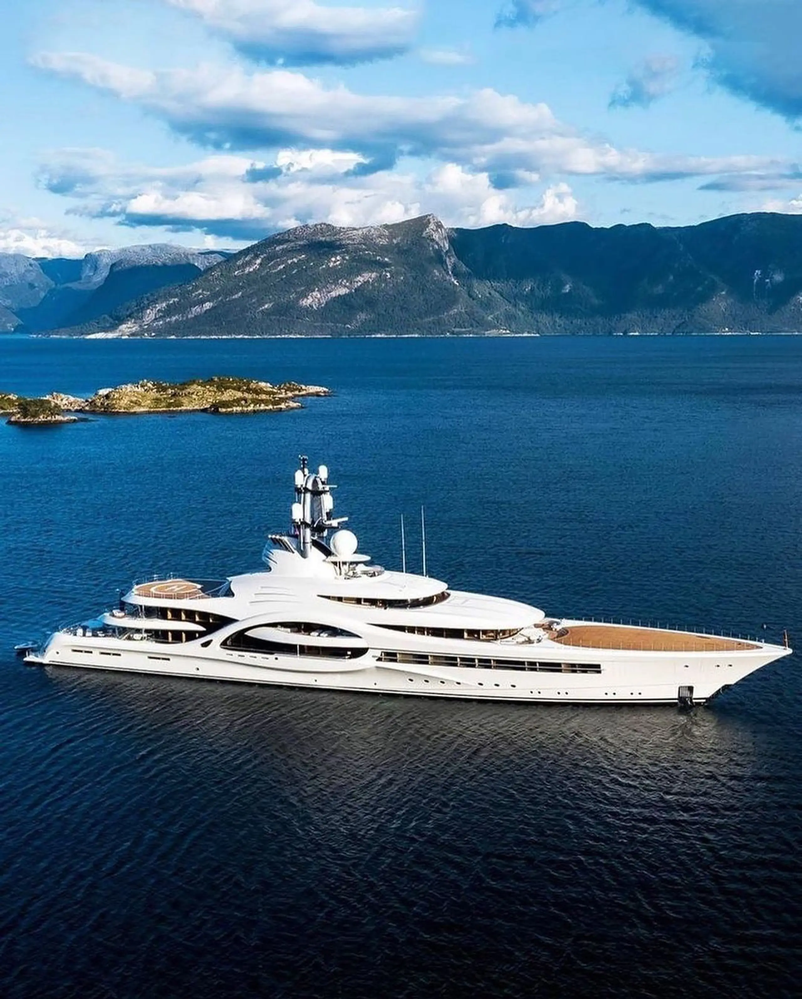 Superyacht anchored in deep blue water with mountains in the background.