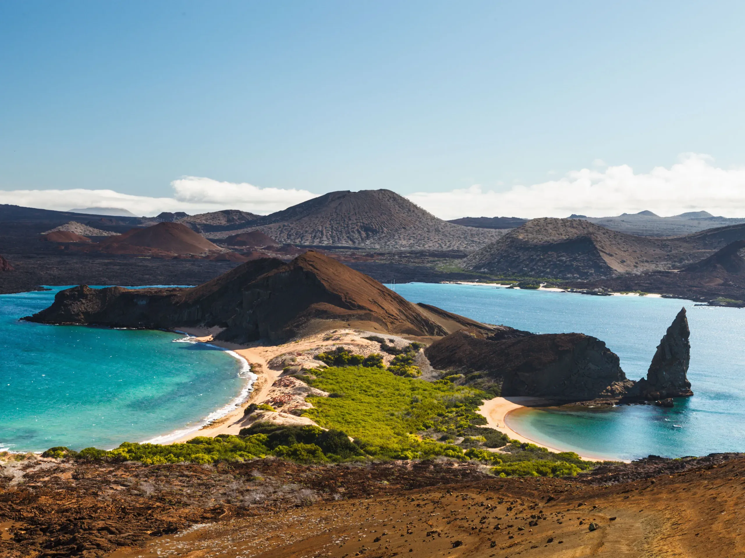 Volcanic coastline and turquoise bays in the Galápagos Islands with arid hills and a distinctive rock formation