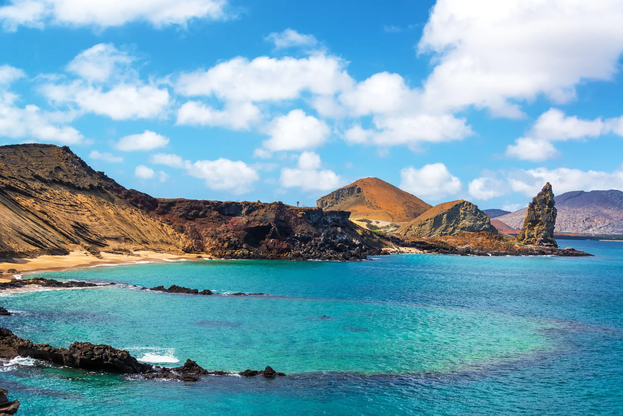 Volcanic coastline and turquoise water in the Galápagos Islands with Pinnacle Rock in the distance