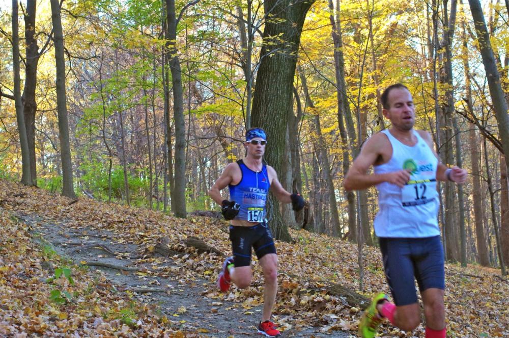 Two runners descending leaf-covered single track in autumn