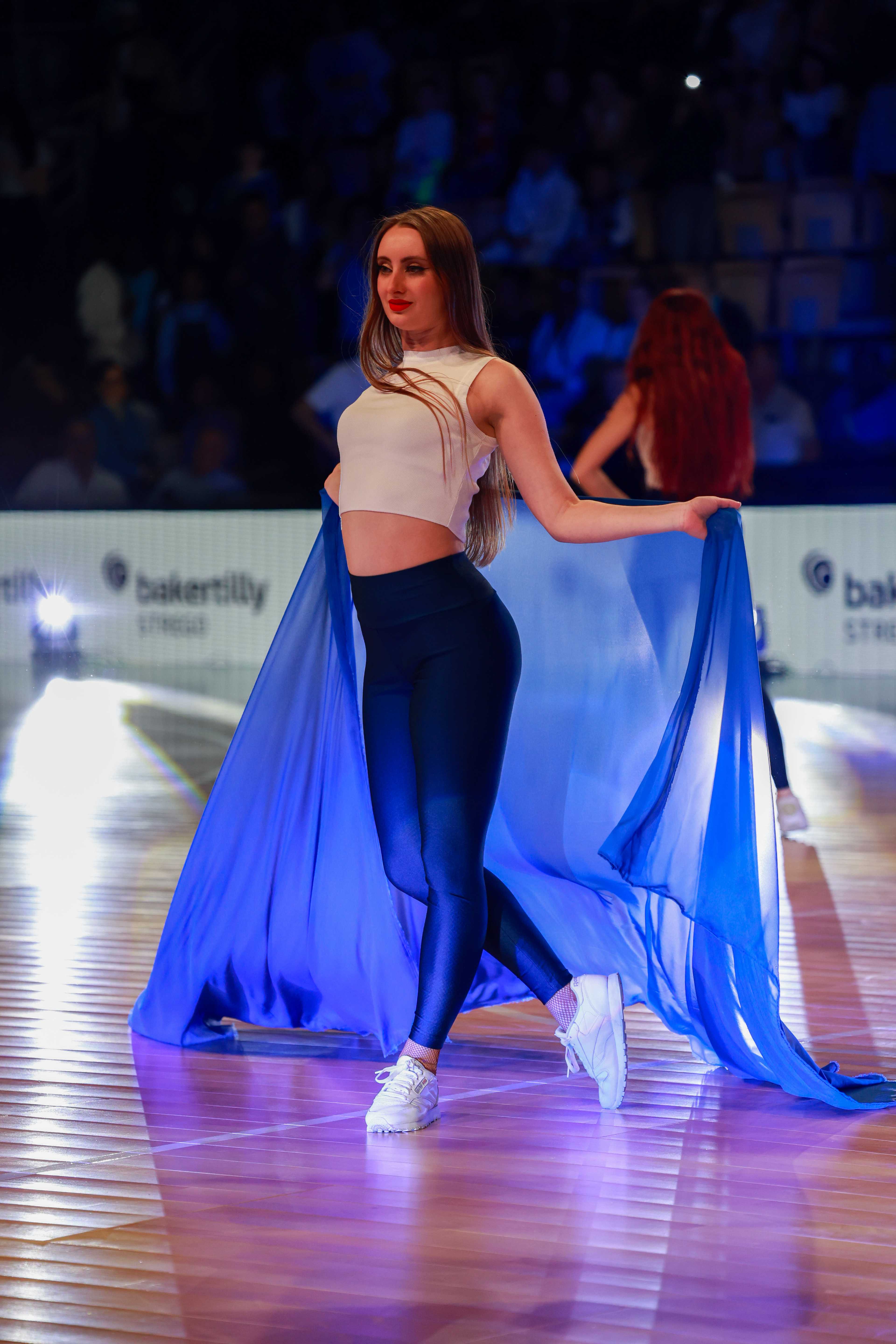 Danseuse déployant un voile bleu translucide sur un parquet de sport