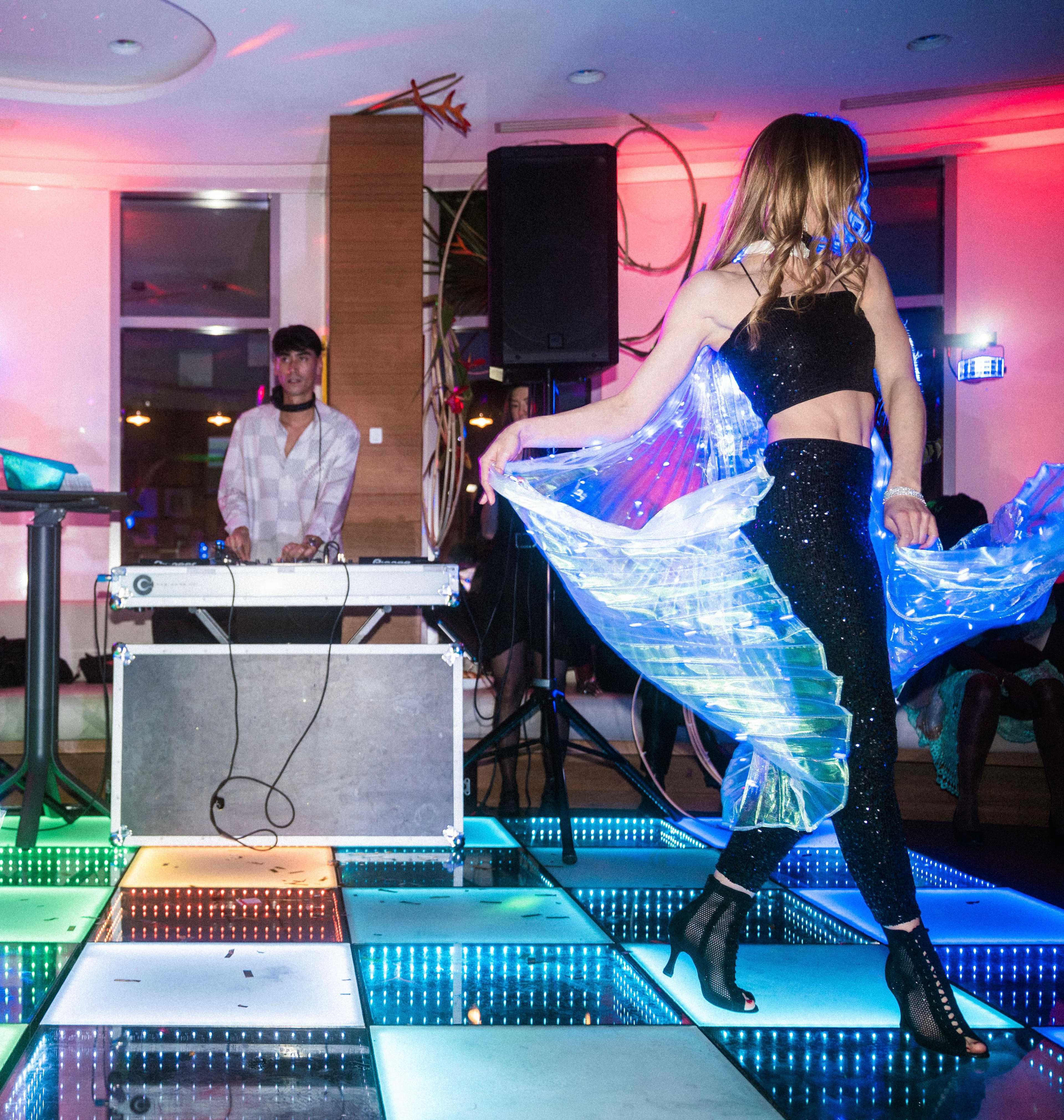 Danseuse de dos, ailes LED déployées, devant la cabine du DJ