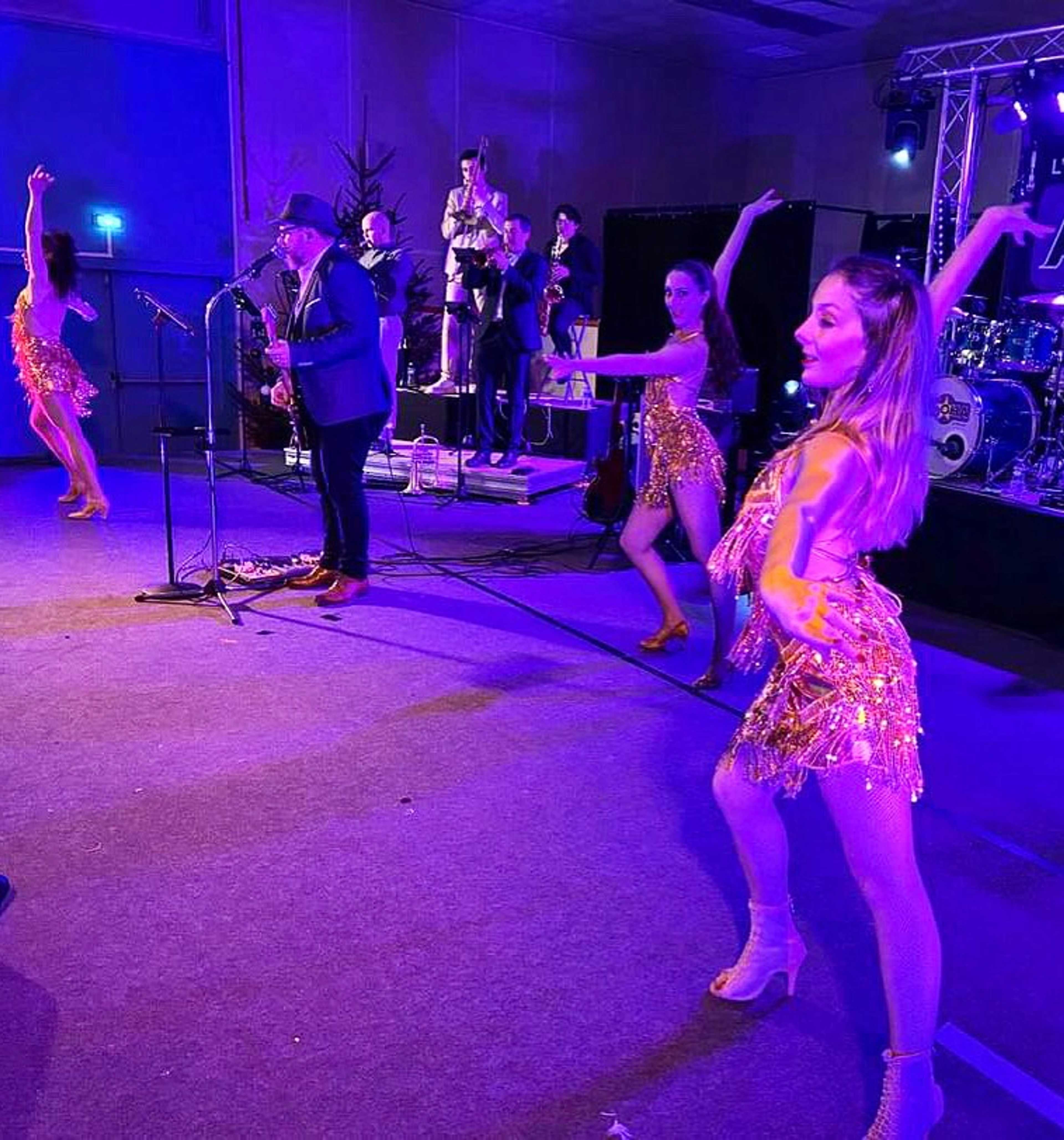 Danseuses en robes à franges dorées devant un orchestre de scène en lumière violette