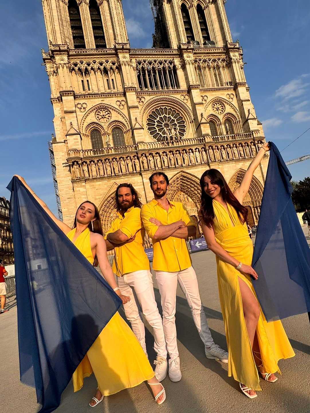 Quatre artistes en tenue jaune tenant des voiles bleus devant Notre-Dame de Paris