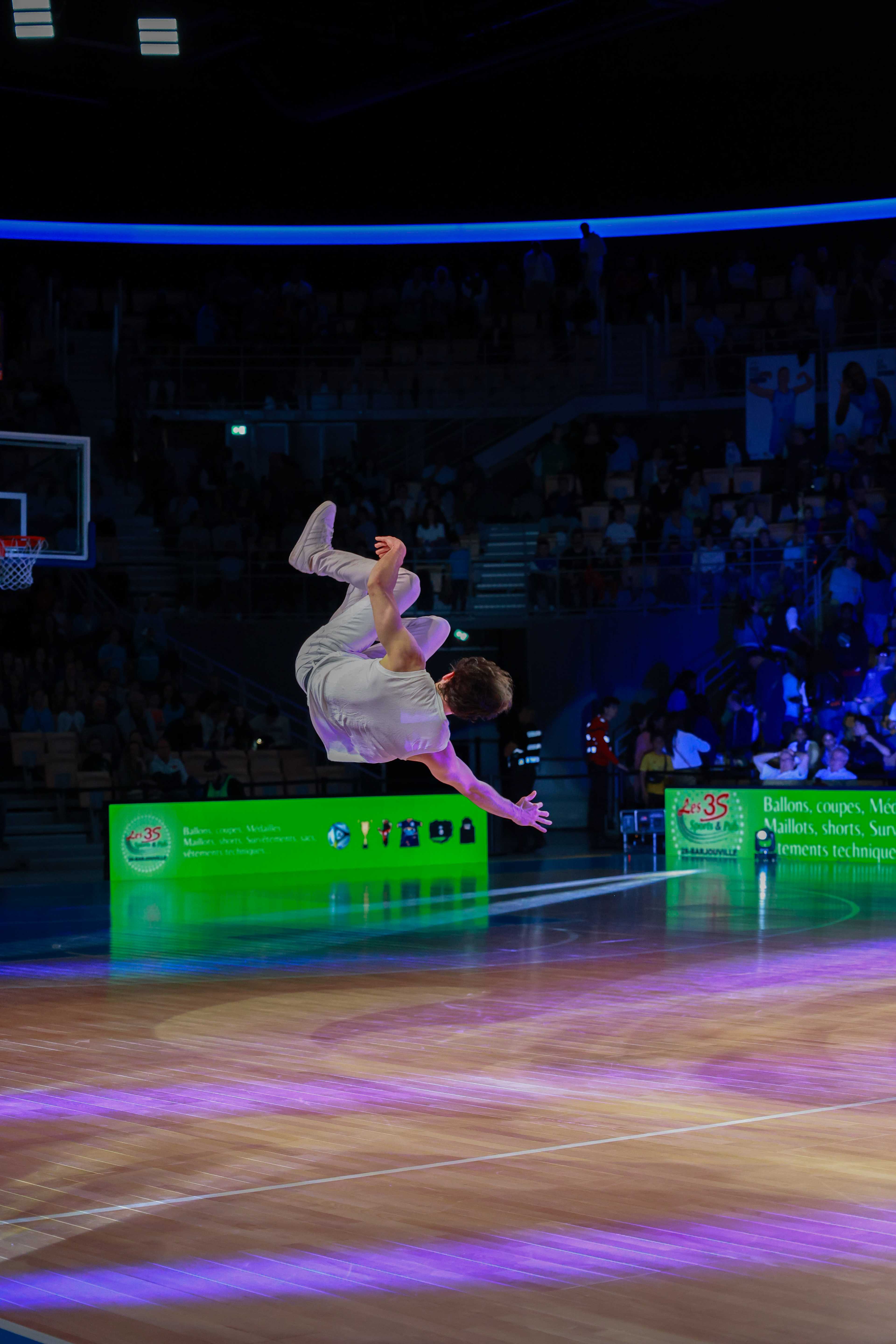 Acrobate en plein salto au-dessus du parquet d'une salle de basket