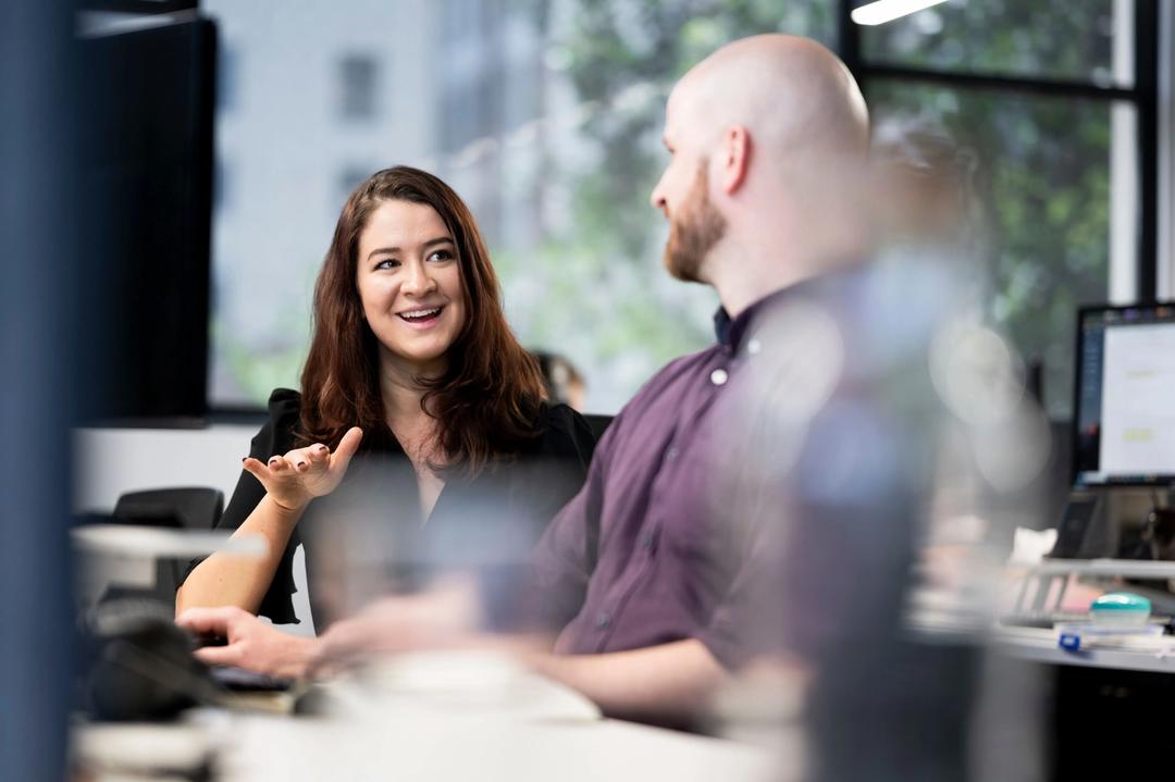 Female enterprise SEO expert smiles while explaining her services to a male collegue.