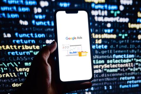 Man holding phone with Google Ads logo against background of HTML code.