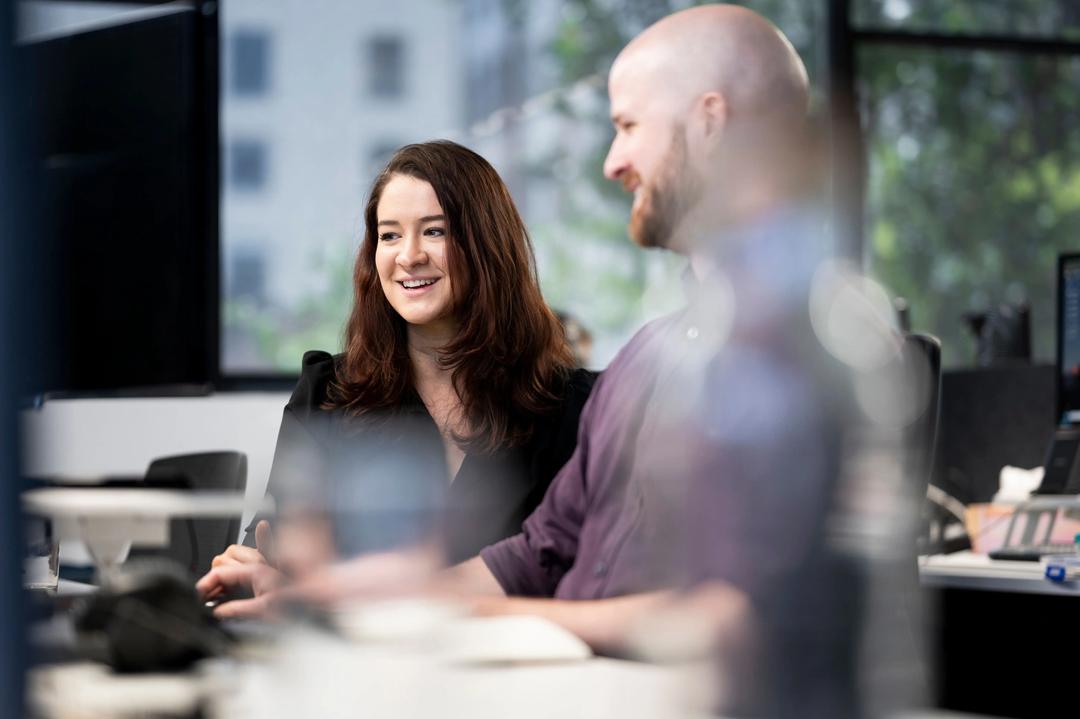 Male and female colleague discussing link building services while smiling at desk.