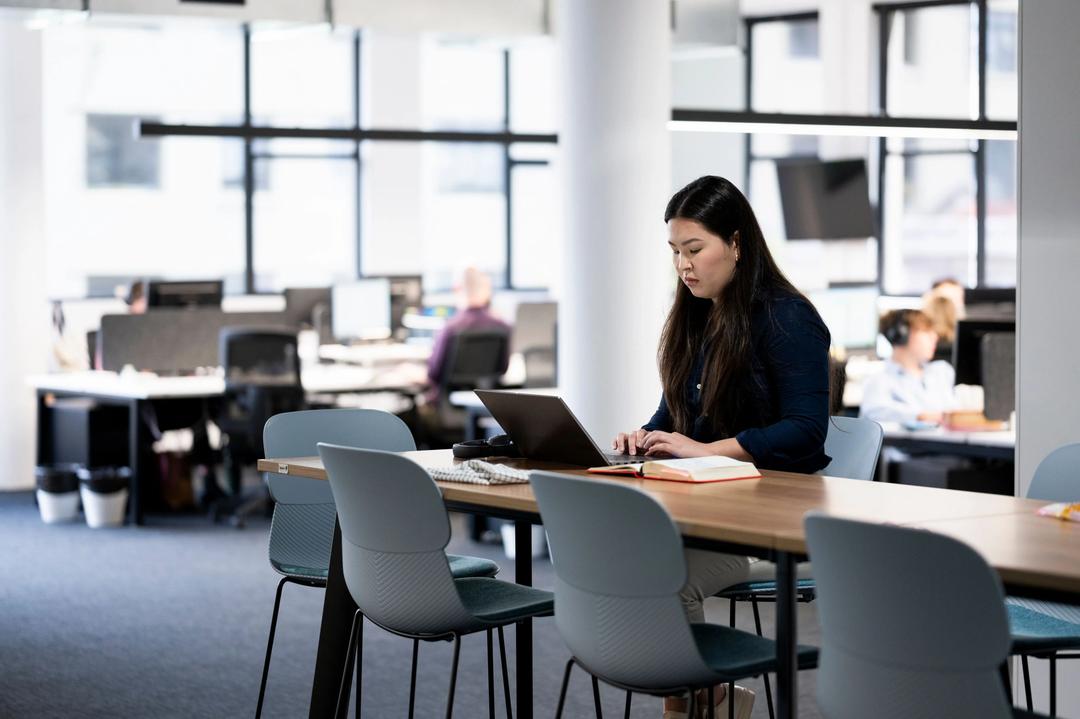 Female SEO content writer working on project on laptop at table in office.
