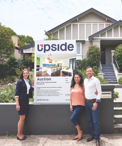 Couple and real estate standing next to upside realty sign.