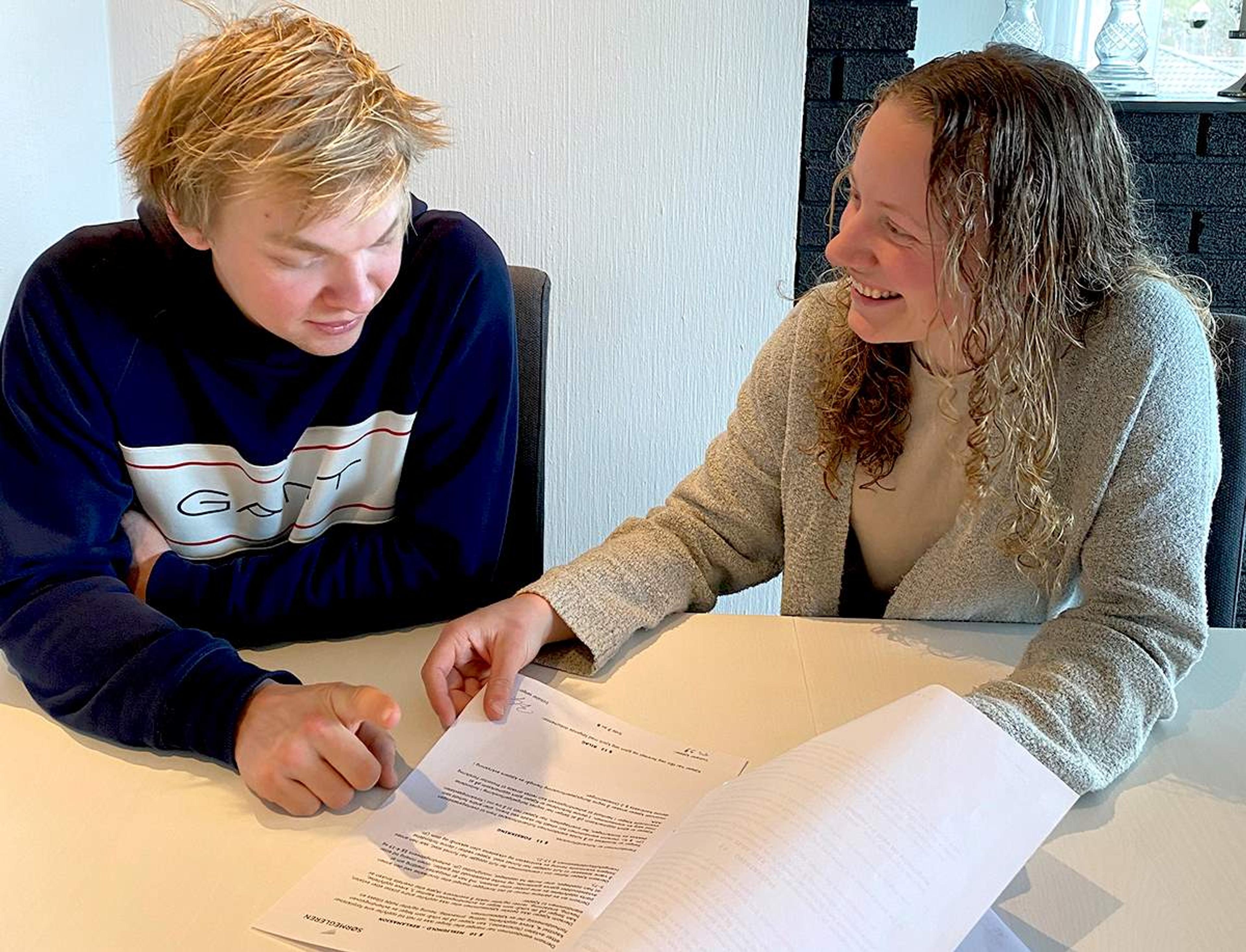 En ung mann og en smilende kvinne sitter ved et bord og ser på et dokument sammen. Kvinnen peker på teksten mens mannen følger med.