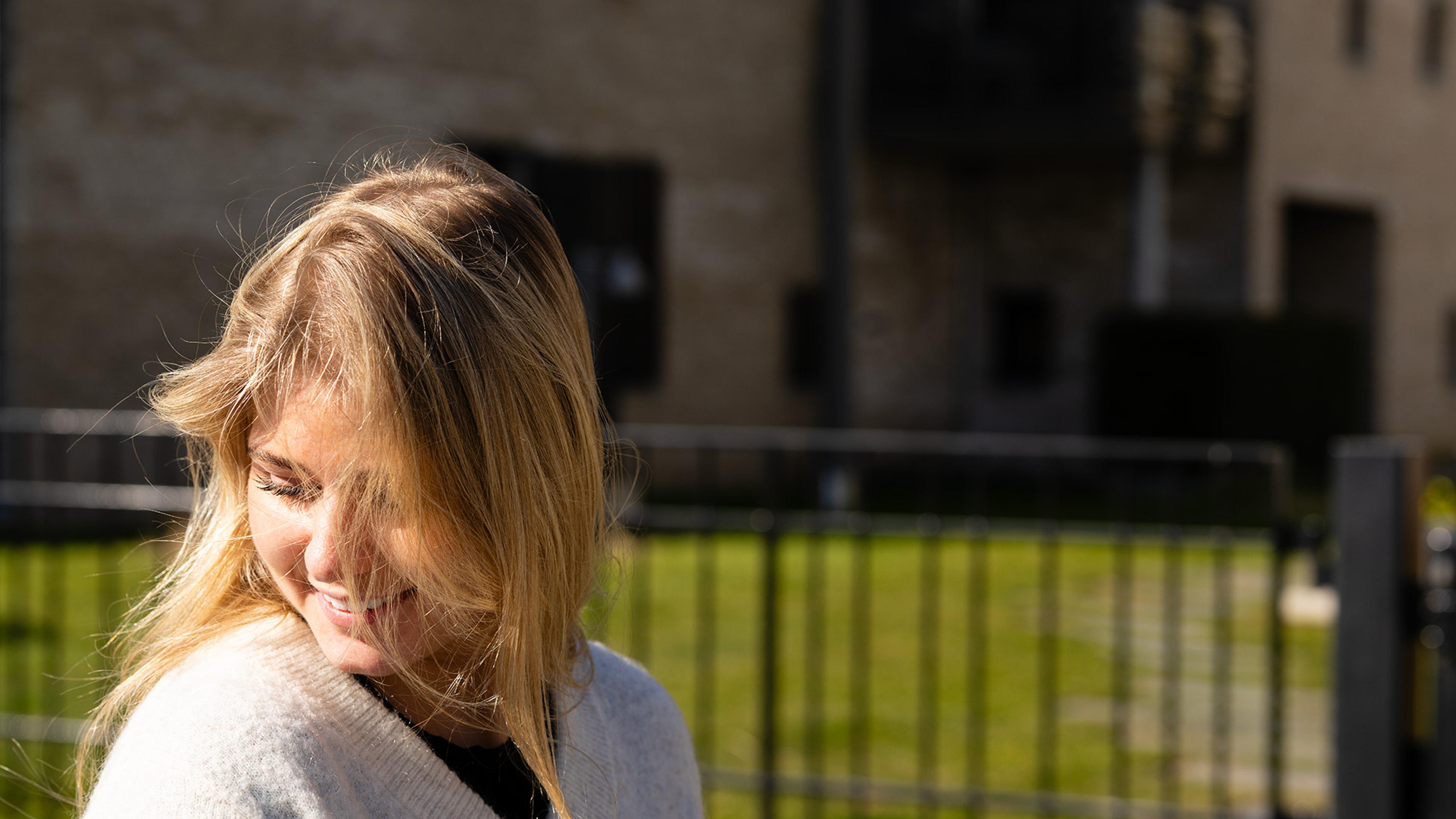 Smilende kvinne med sol i ansiktet på venstre side i bildet 