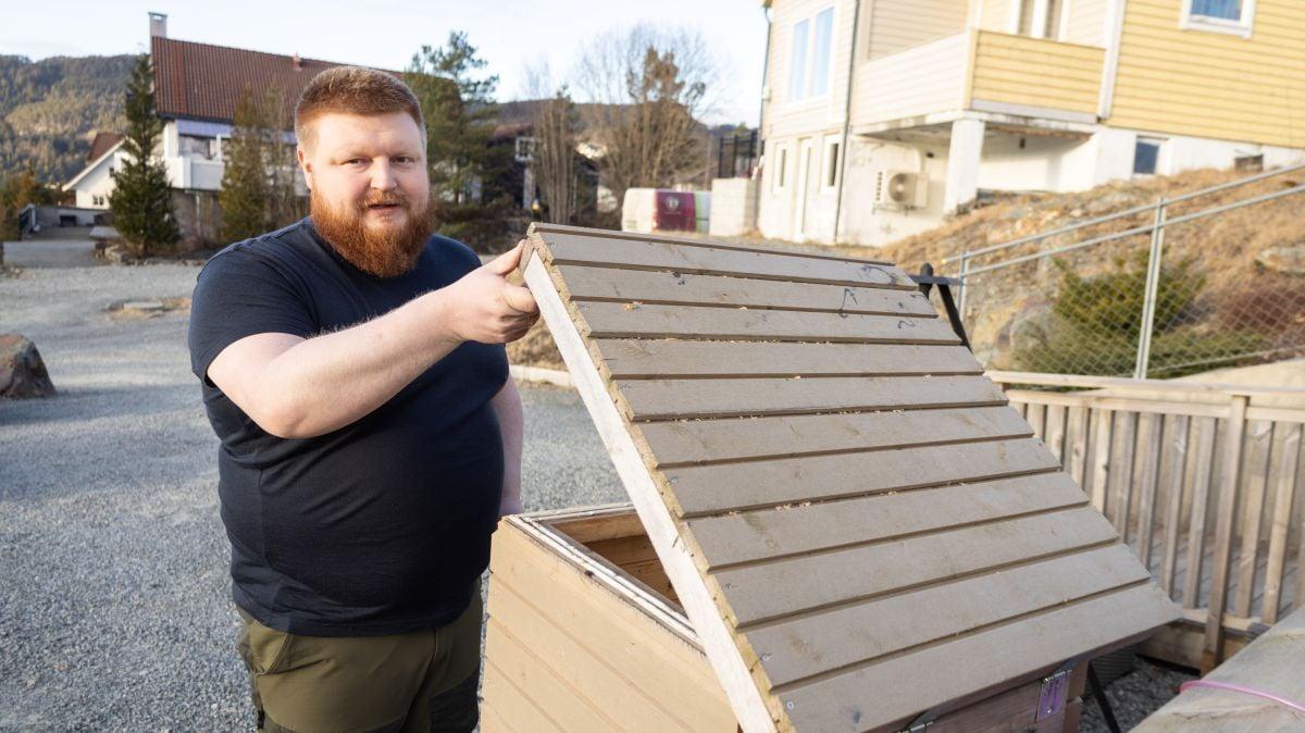Mann som står oppstil og holder oppe et lokk på en kasse