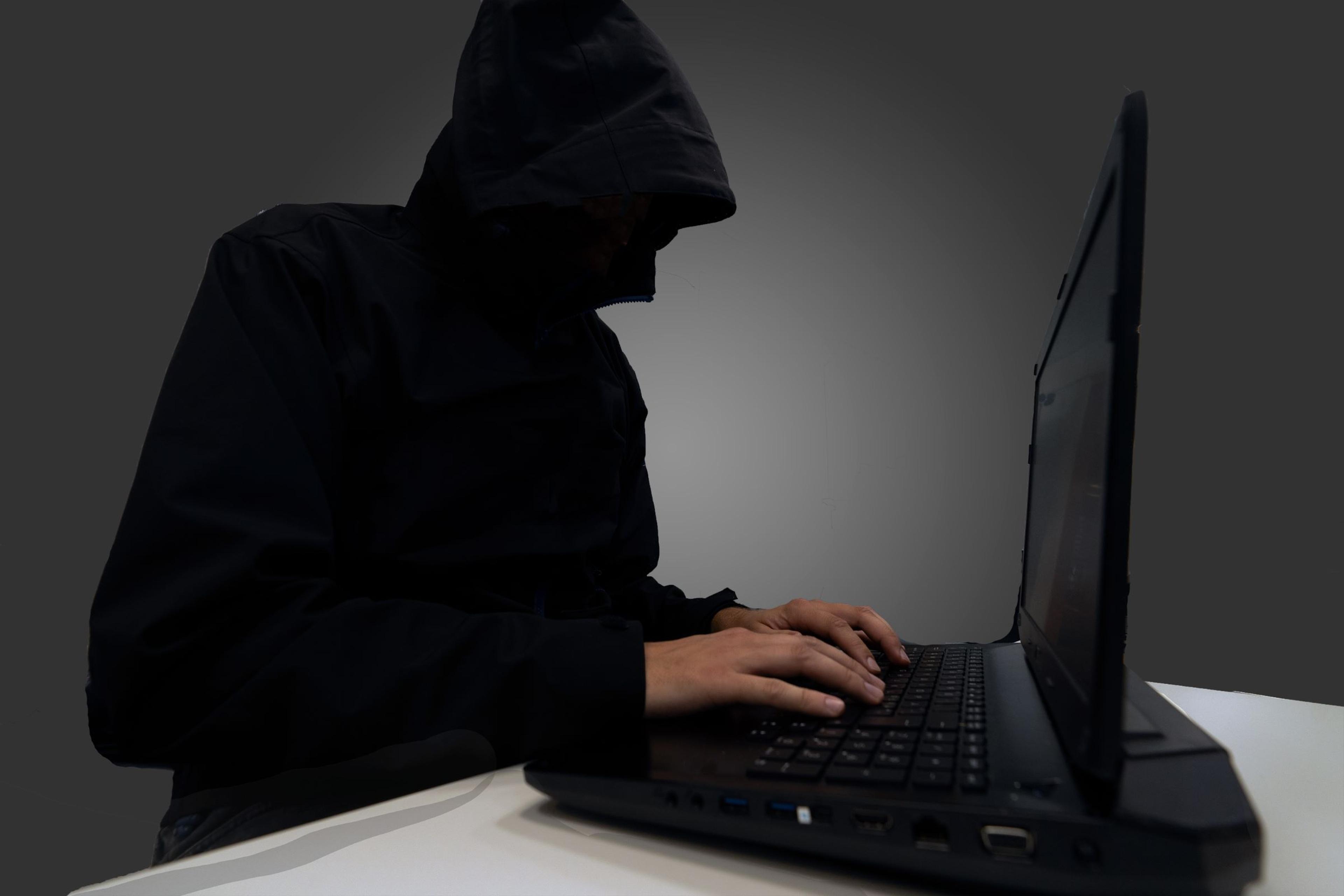 Person som sitter foran laptop, skjult under mørk hettejakke