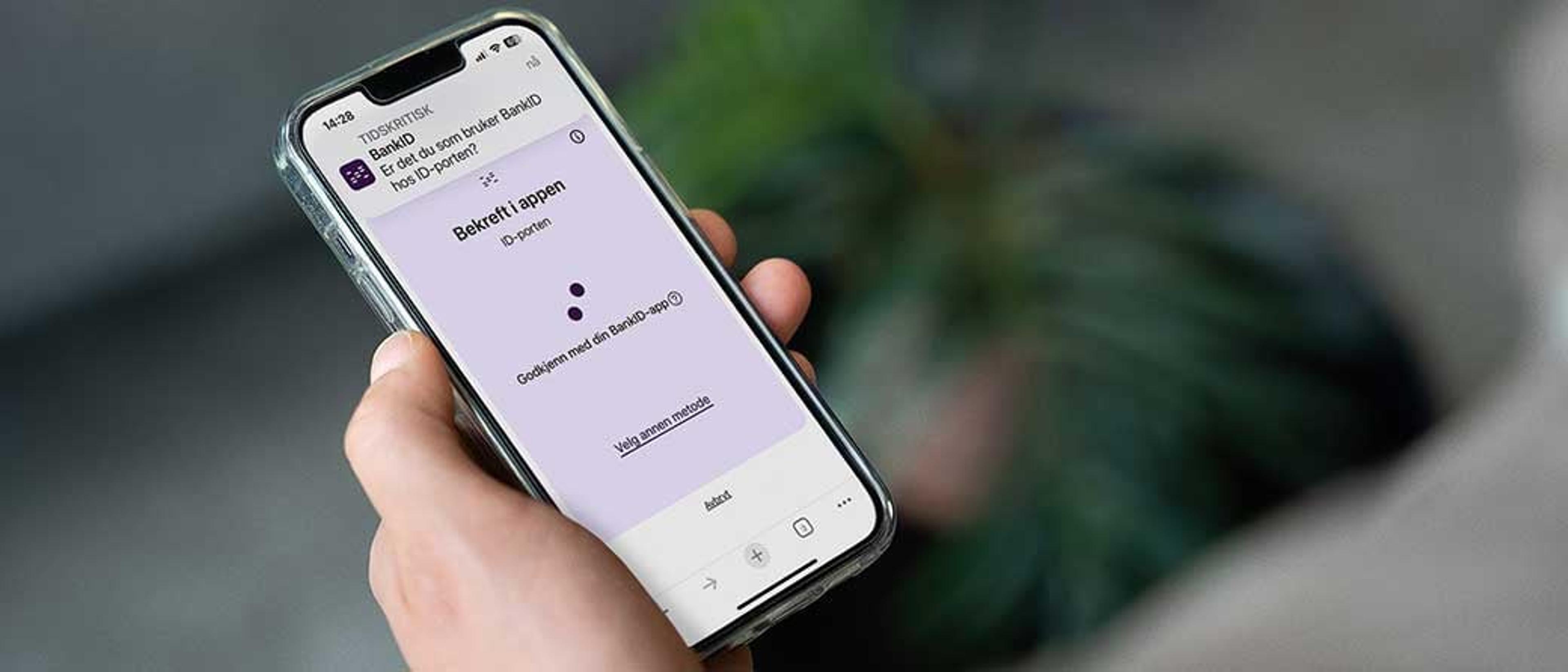 Hånd som holder en mobiltelefon, med skjermbilde fra BankID-appen