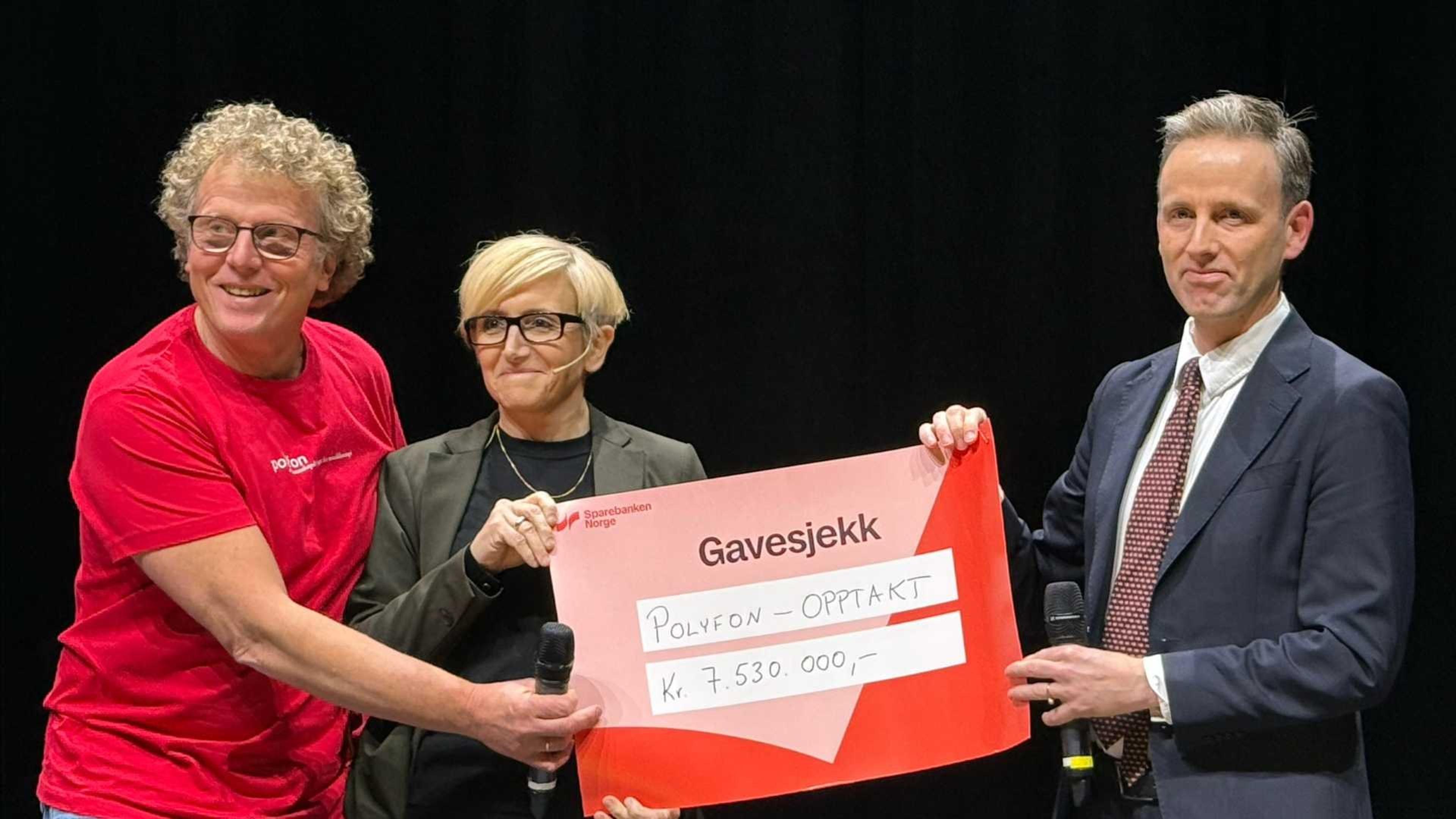 Tre personer på en scene holder en stor gavesjekk fra Sparebanken Norge til Polyfon-opptakt på 7 530 000 kroner.