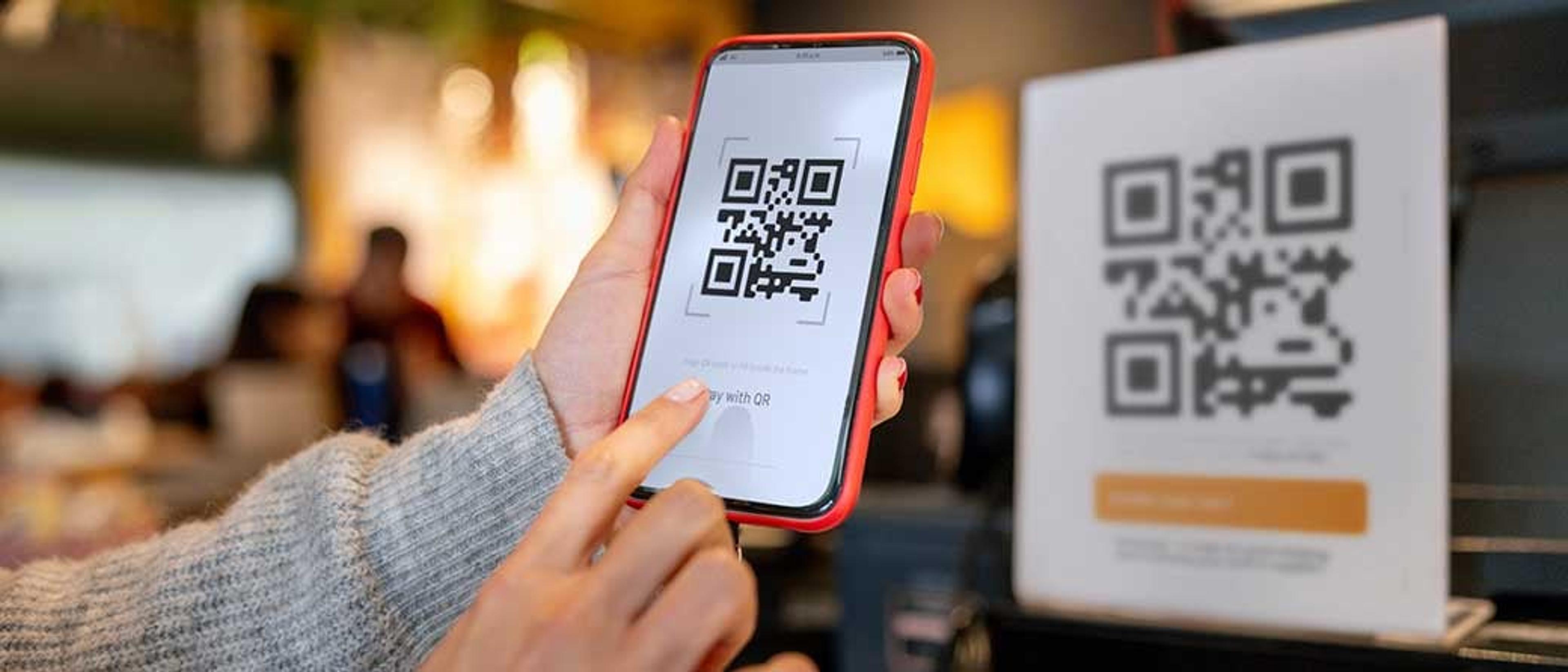 Hender holder en mobiltelefon opp og tar bilde av en QR-kode