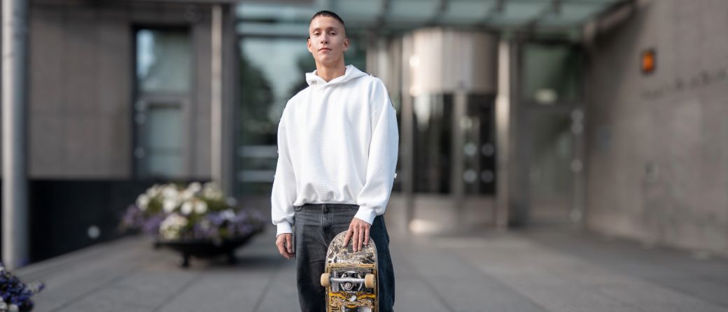 Ung mann med svart jeans og hvit hettegenser som holder på et skateboard