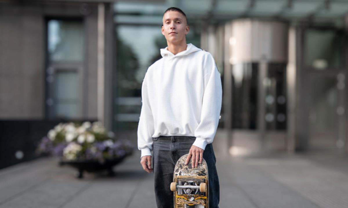 Ung mann med svart jeans og hvit hettegenser som holder på et skateboard