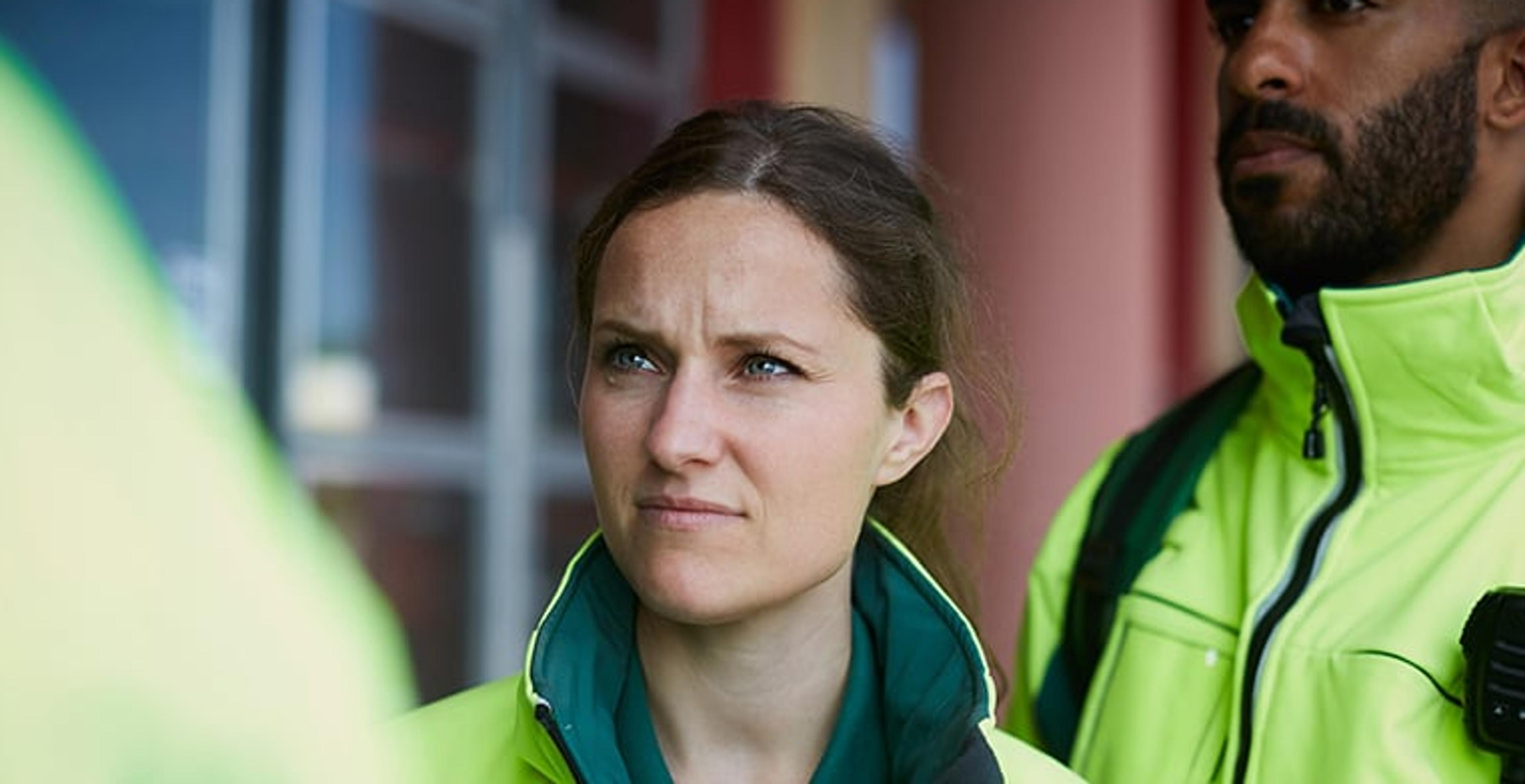To redningsarbeidere i neongule uniformer lytter alvorlig til en person utenfor bildet. Mannen til høyre har en radiosender festet til uniformen.