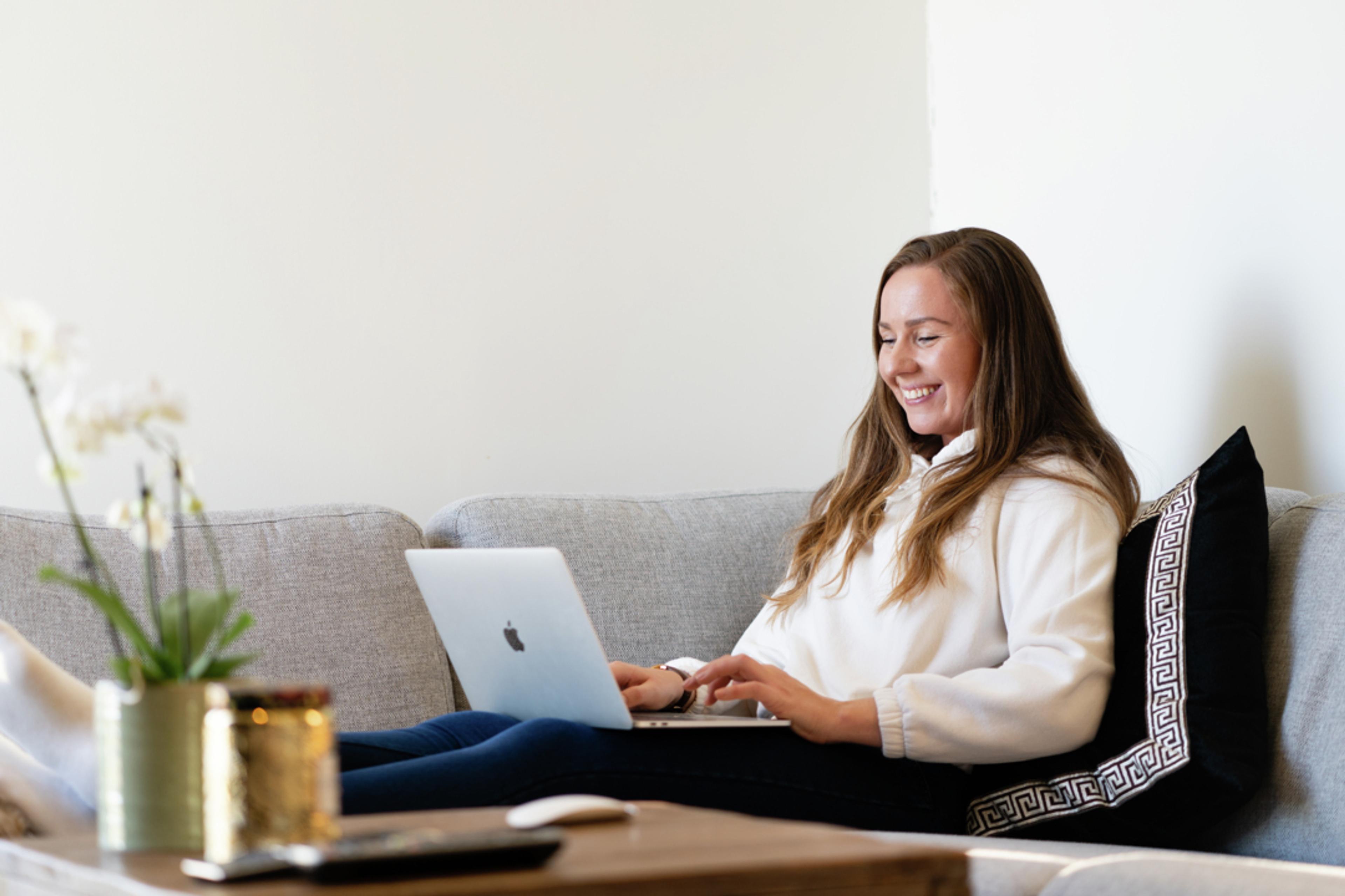 Kvinne sitter i sofaen med datamaskin på fanget.