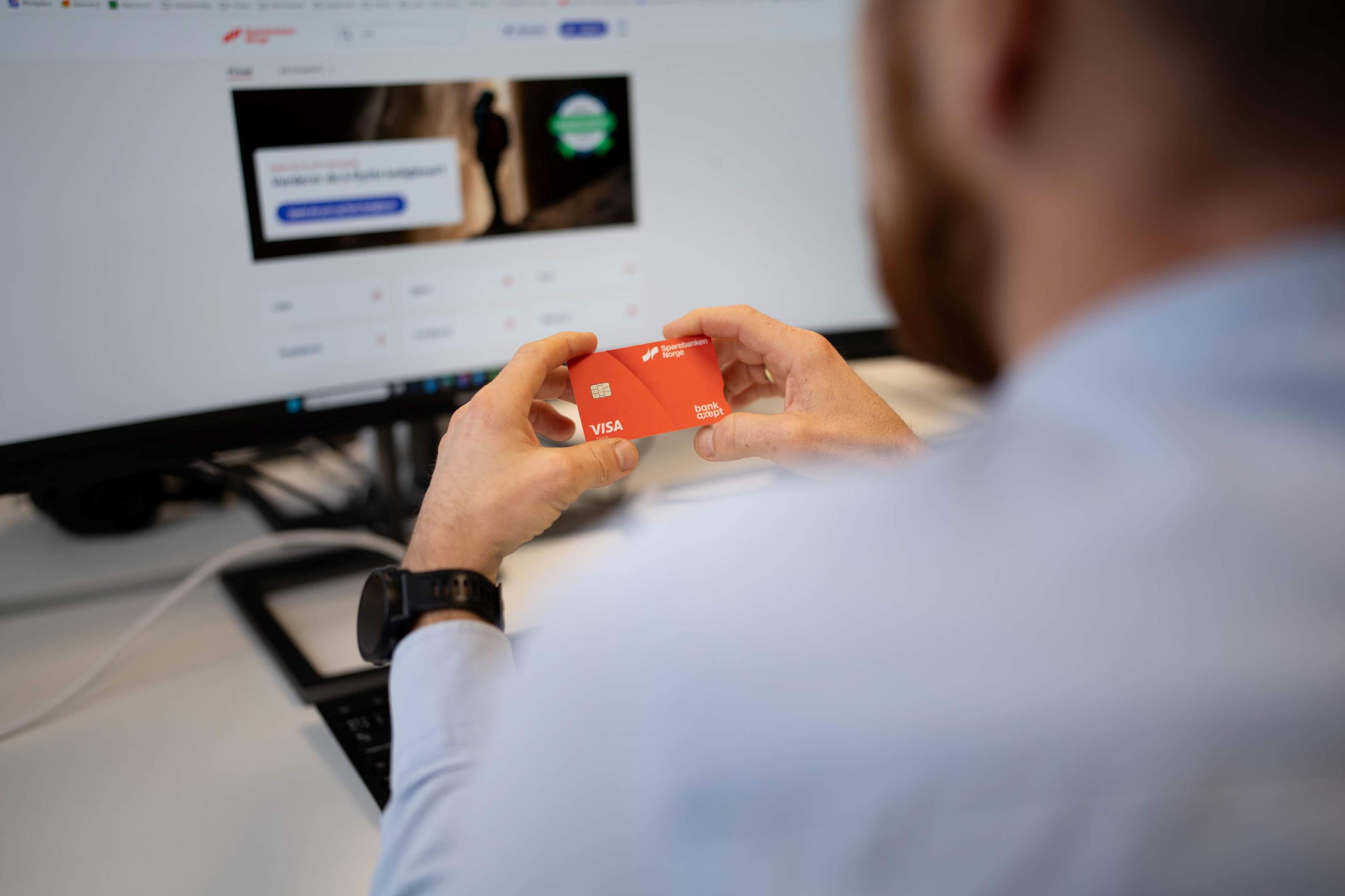 Bilde av mann som holder kortet i hendene foran en PC.