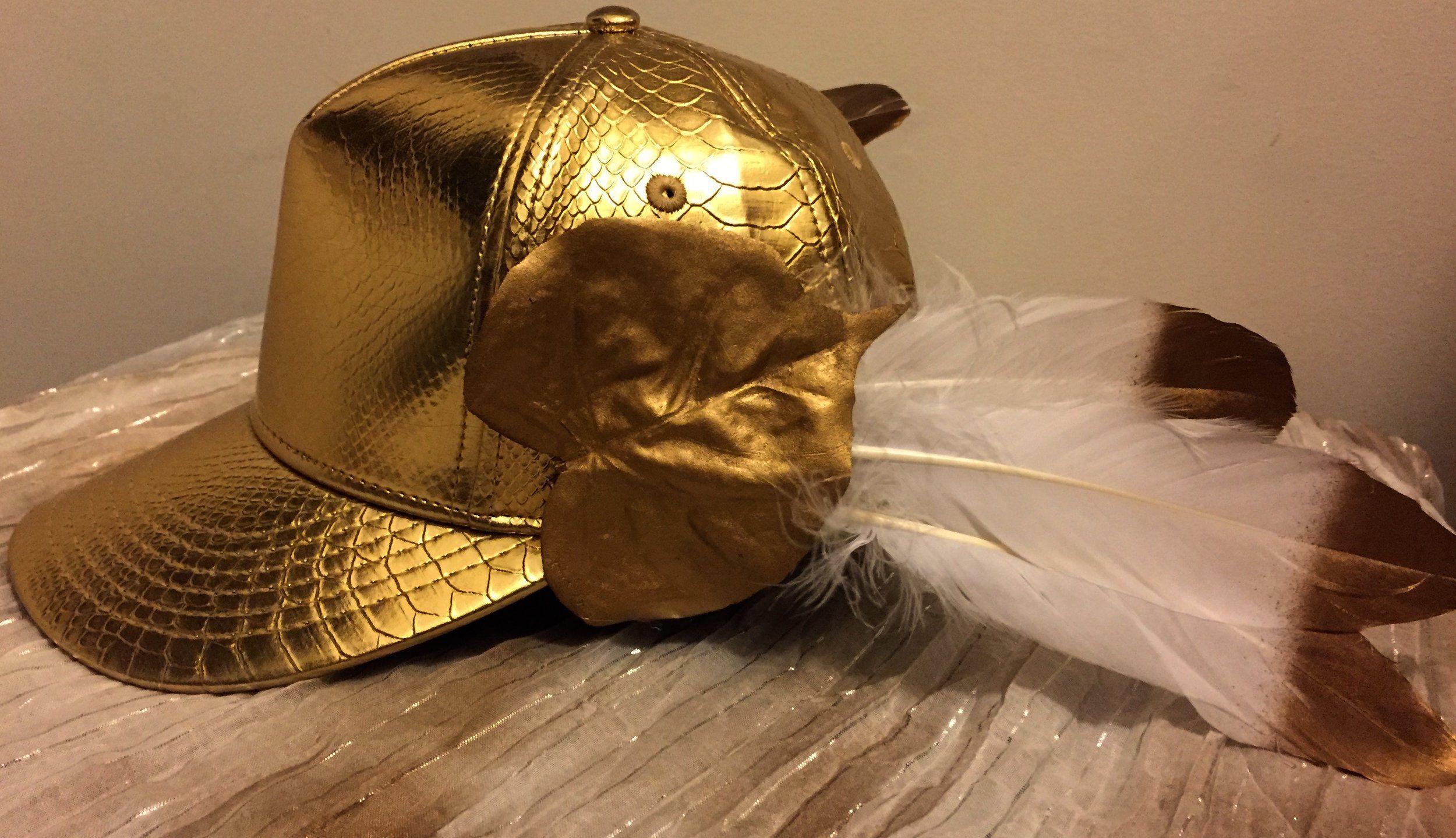 A gold baseball cap, with feathers attached