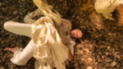 julie in white, covered in a sheet, laying face up in dead leaves