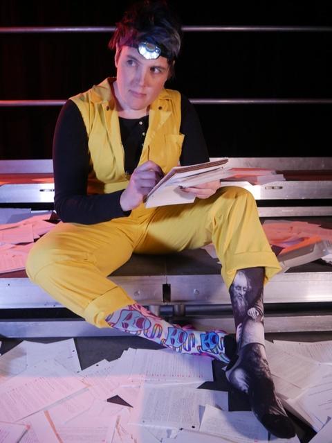 Mia in yellow coveralls and a headlamp, surrounded by paper, writing and looking into the distance