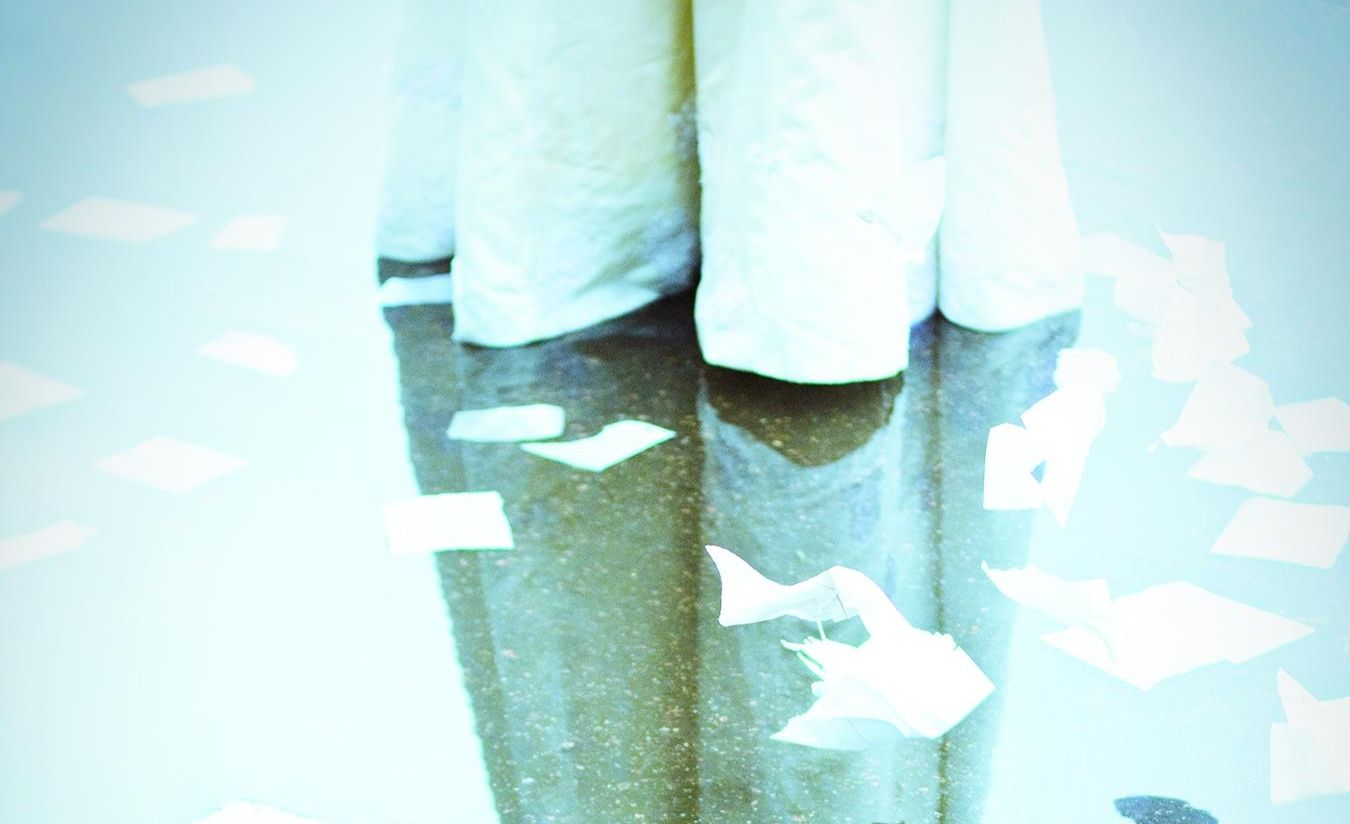 the hem of a wedding gown, standing in a puddle, with floating scraps of paper