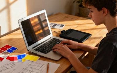 Young design student working on graphic design project with multiple tools and devices on desk