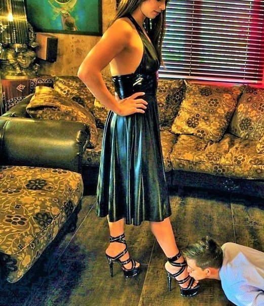 Парень целует ноги девушки в босоножках. Девушка одета в сексуальное латексное платье