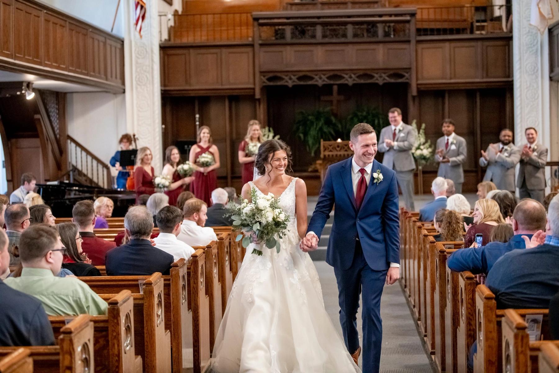 Hanna and Nathan walk hand in hand down the sanctuary aisle past their guests