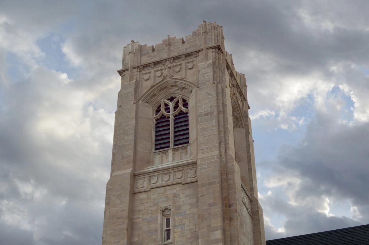 The limestone bell tower rises against a sky of scattered clouds, seen from a low angle.