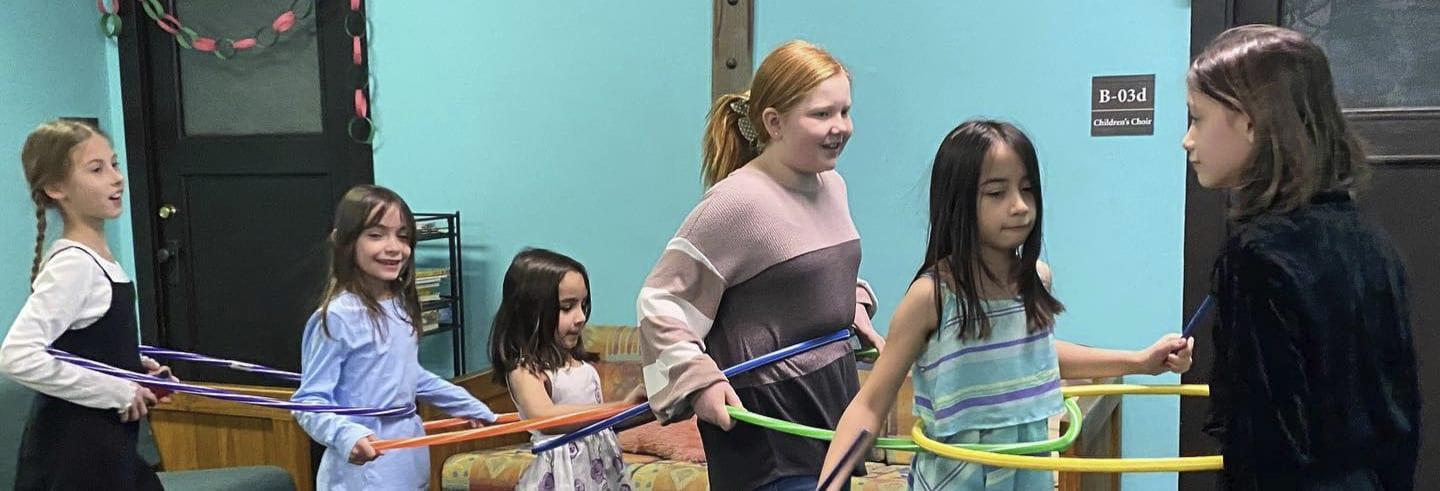 Children playing a group game with a long ribbon or hoop in a classroom.