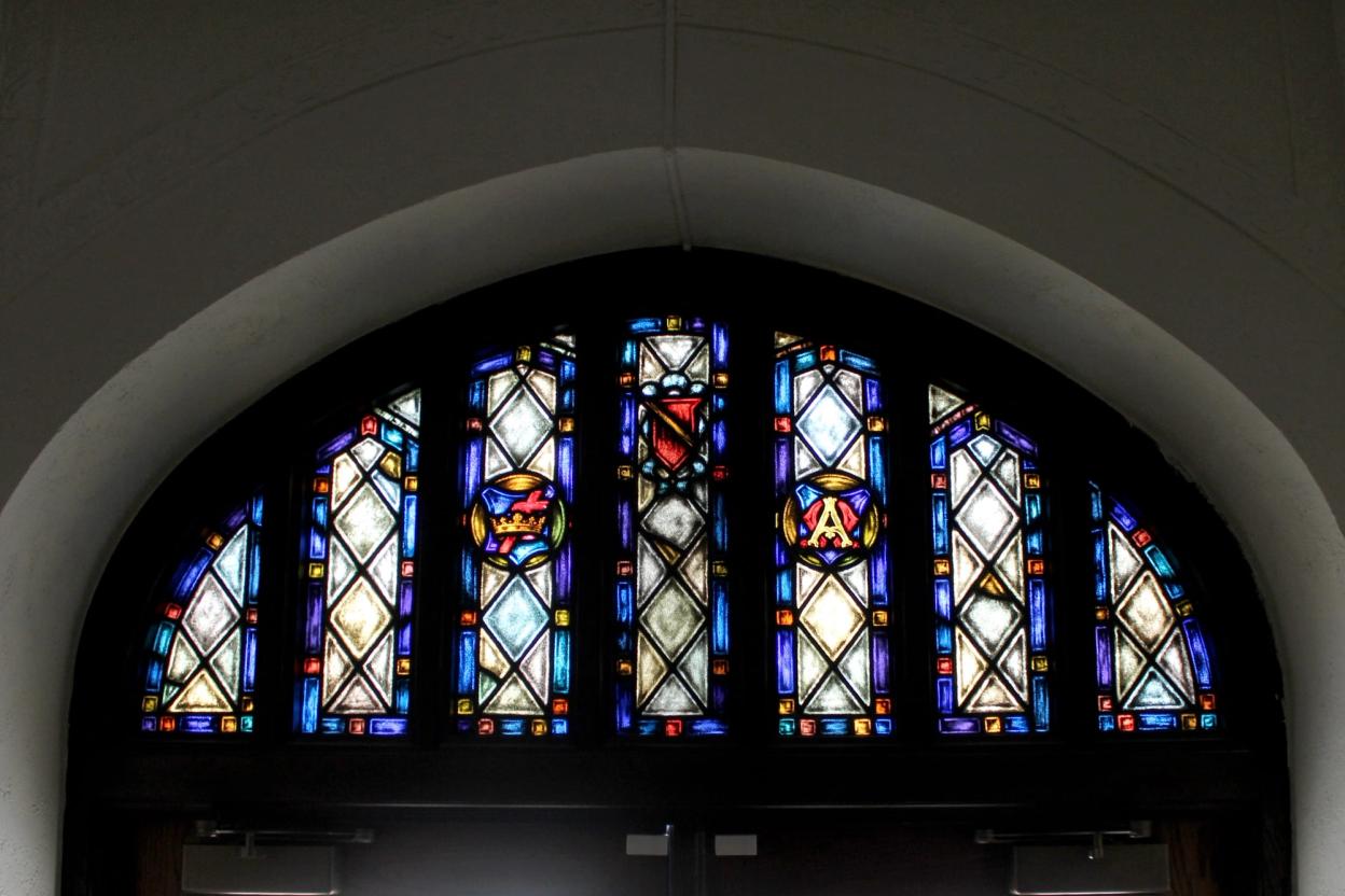 A row of narrow arched stained glass windows glows above a doorway inside the church.