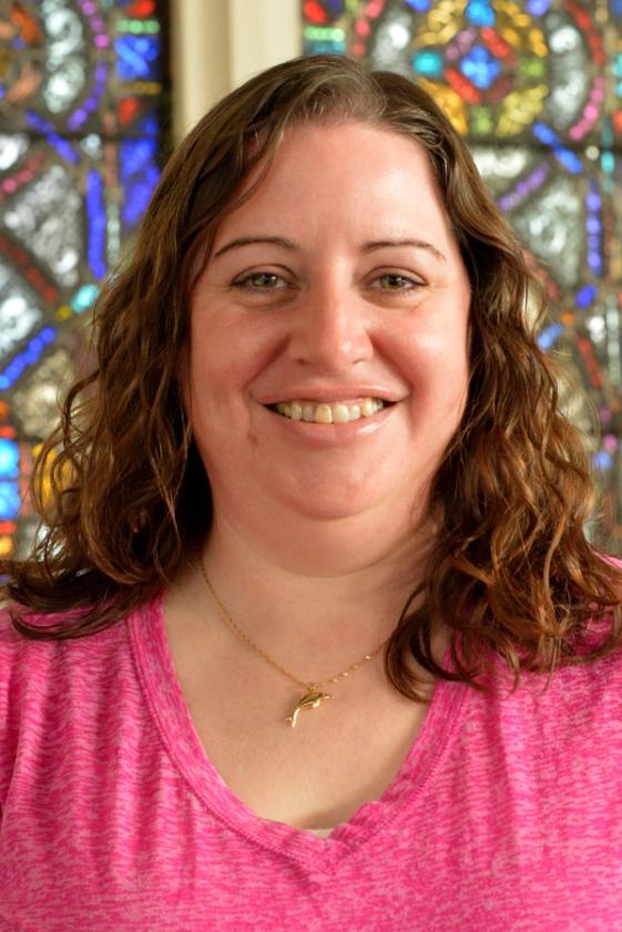 A woman in a pink top smiles for a staff portrait, with colorful stained glass filling the background.